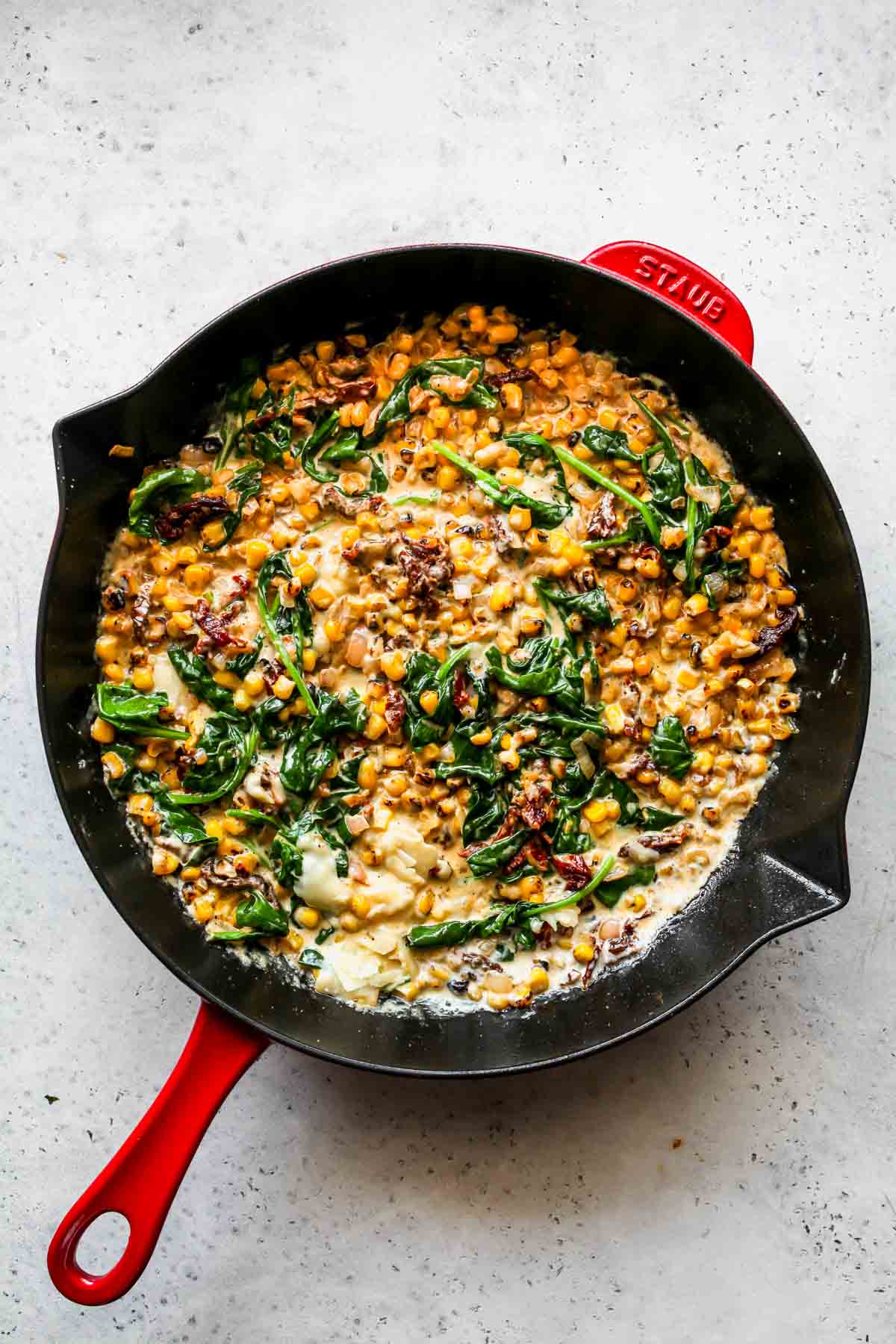 Heavy cream and Parmesan being added to a skillet of veggies