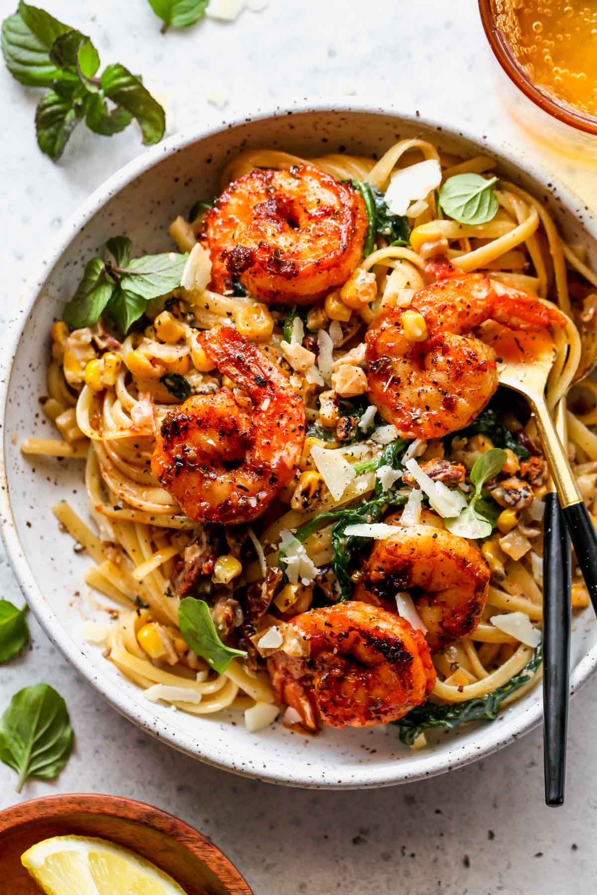 Shrimp and corn pasta in a white bowl topped with fresh basil leaves.