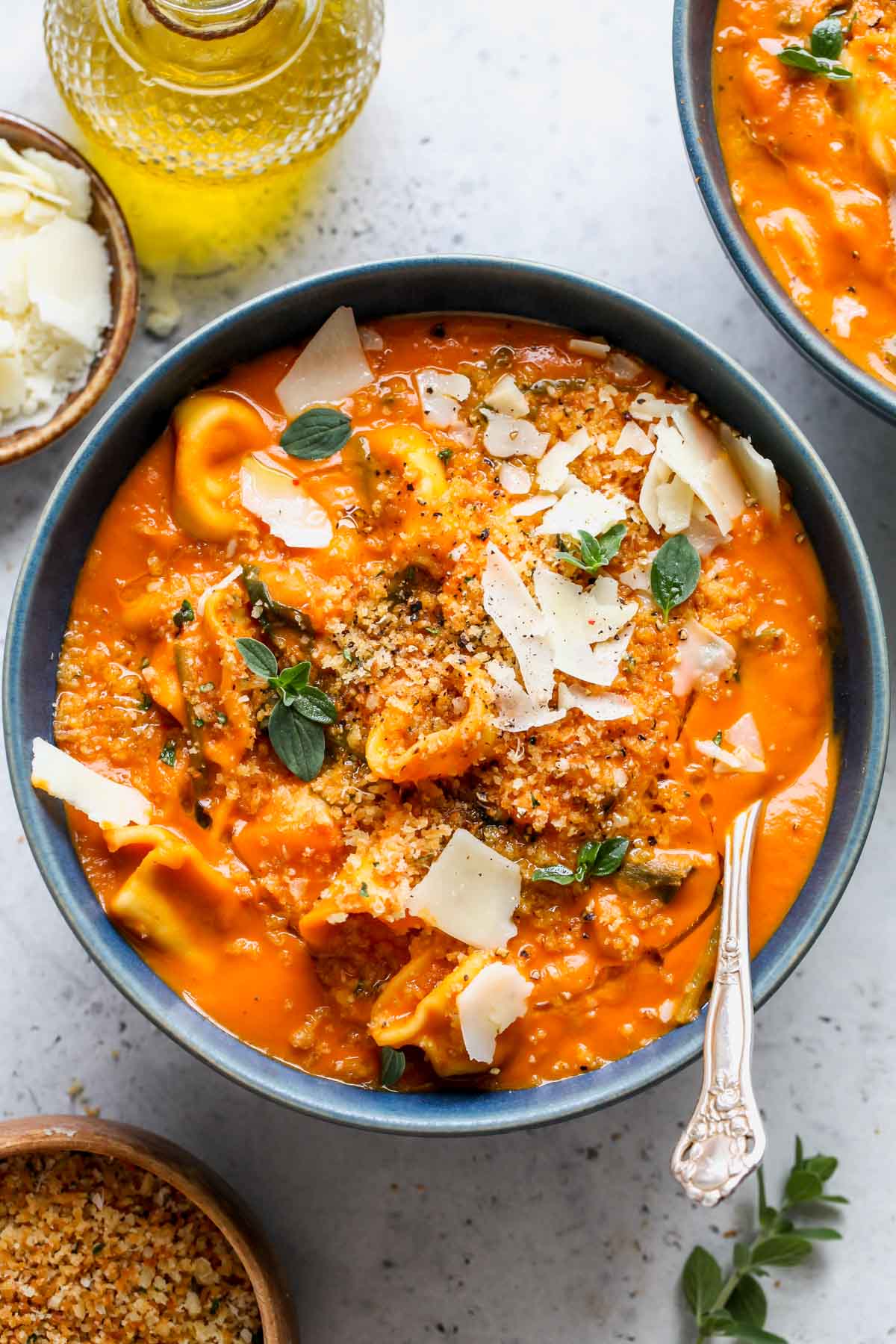 Creamy tortellini soup topped with herbs and crispy oregano breadcrumbs in a blue bowl.