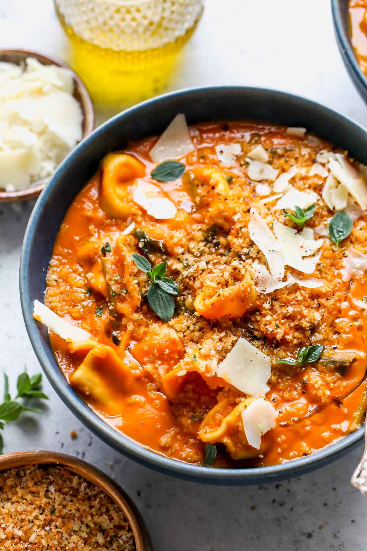 Creamy Spinach Tortellini Soup topped with oregano breadcrumbs in a blue bowl.