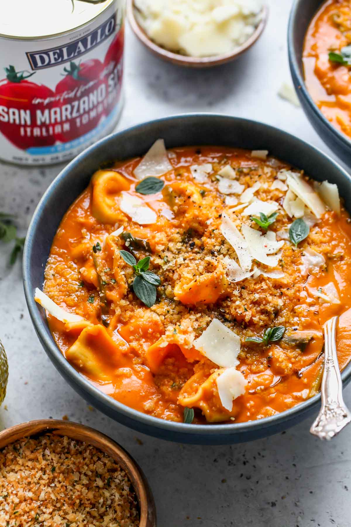 Creamy tortellini soup in a blue serving bowl with a spoon resting on the right side.