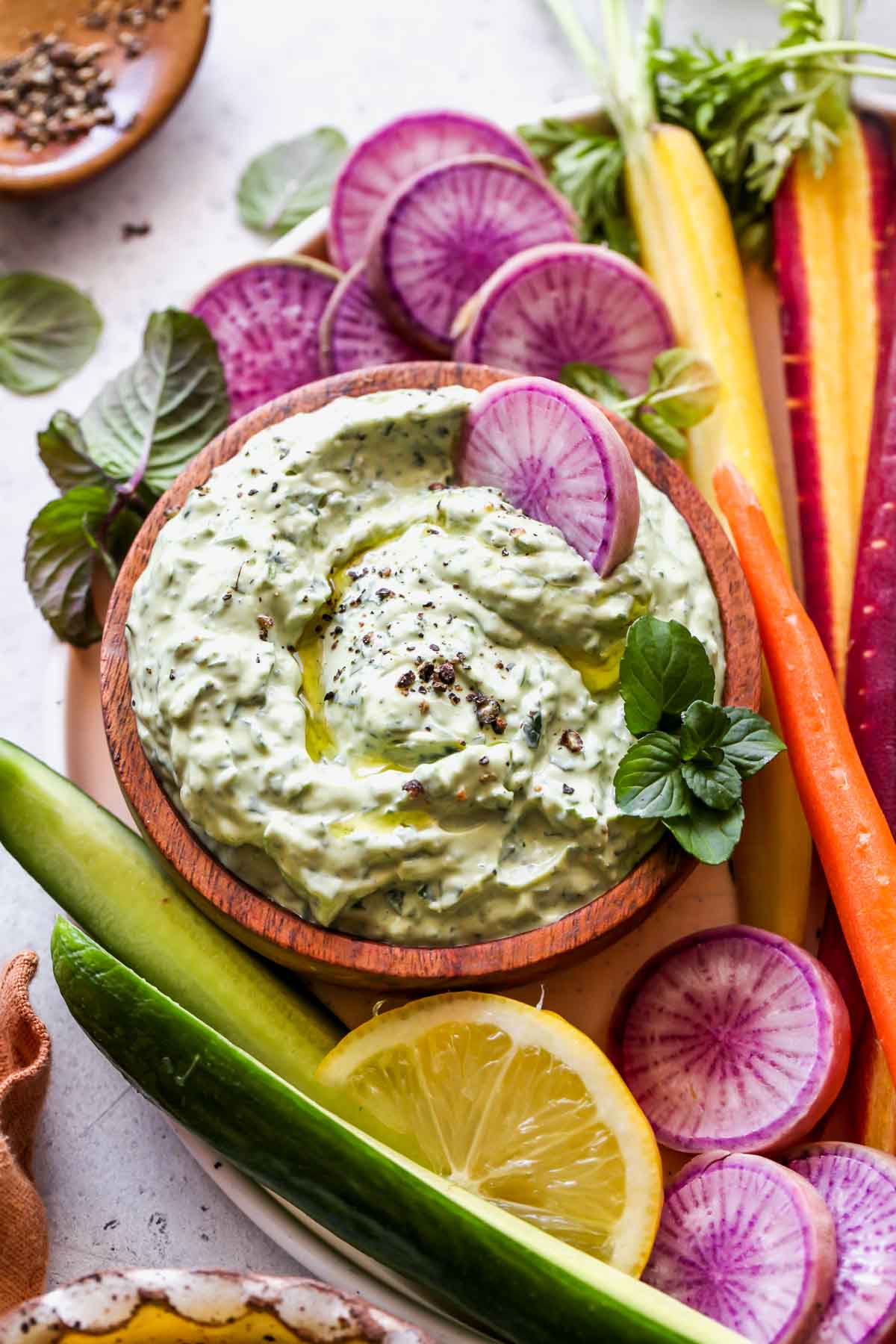 Radish slice being dipped into a bowl of green goddess dip