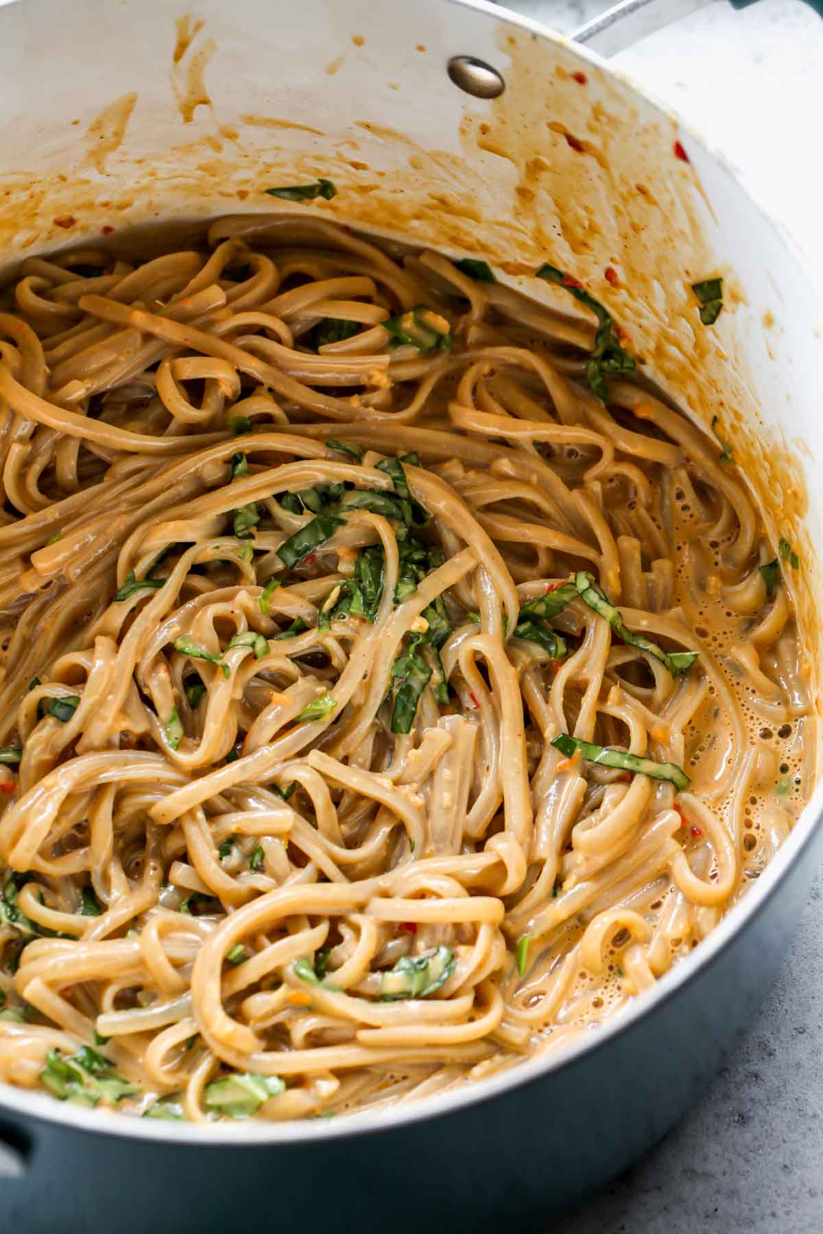 Peanut sauce being added to noodles in a pot