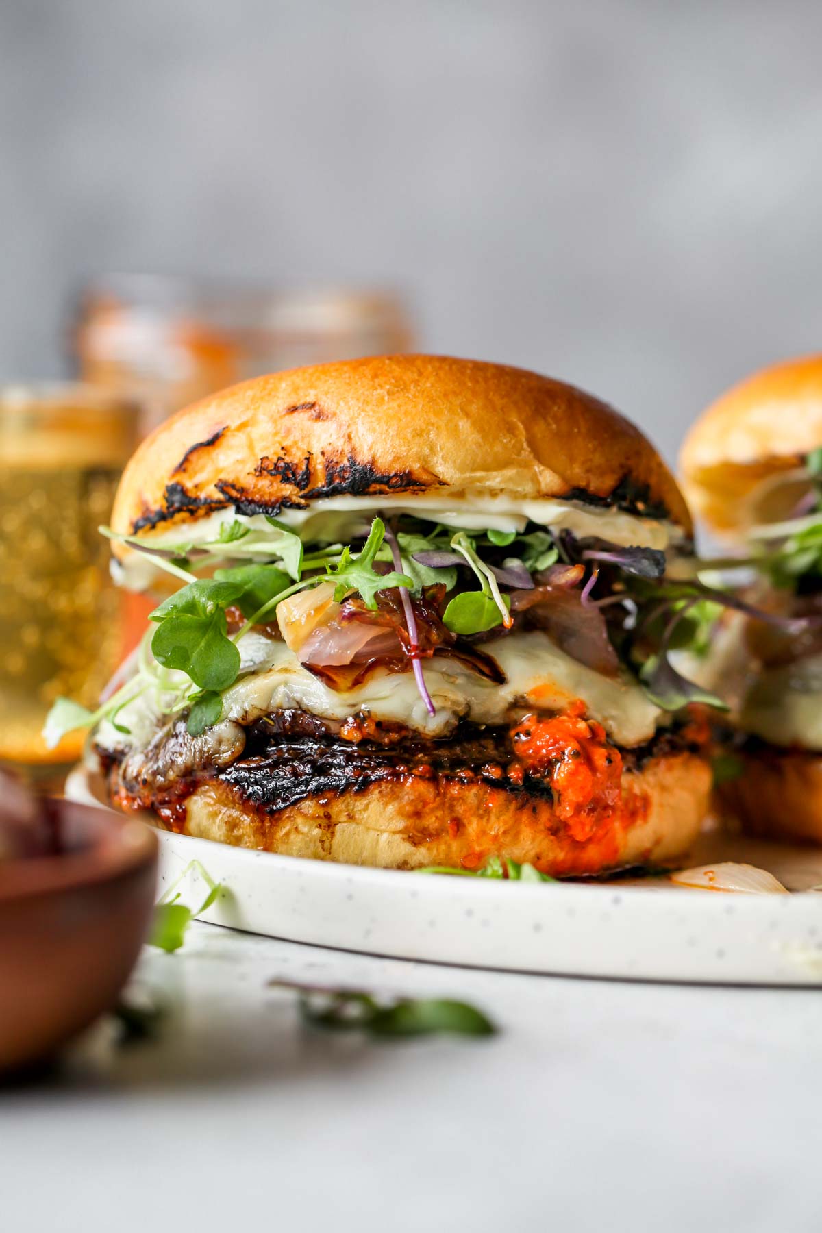 Portobello Burger topped with cheese, romesco cheese, and microgreens on a plate