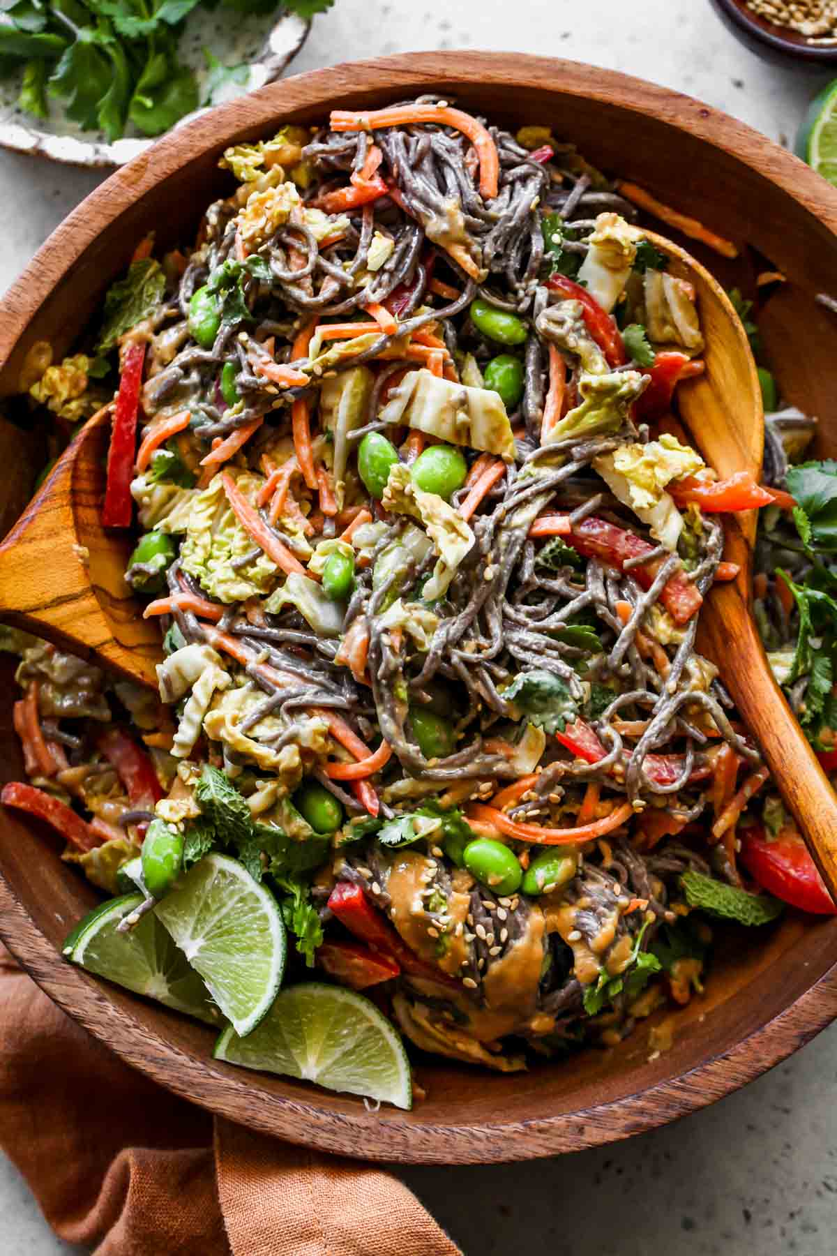 Vegan soba noodle salad being tossed in a mixing bowl