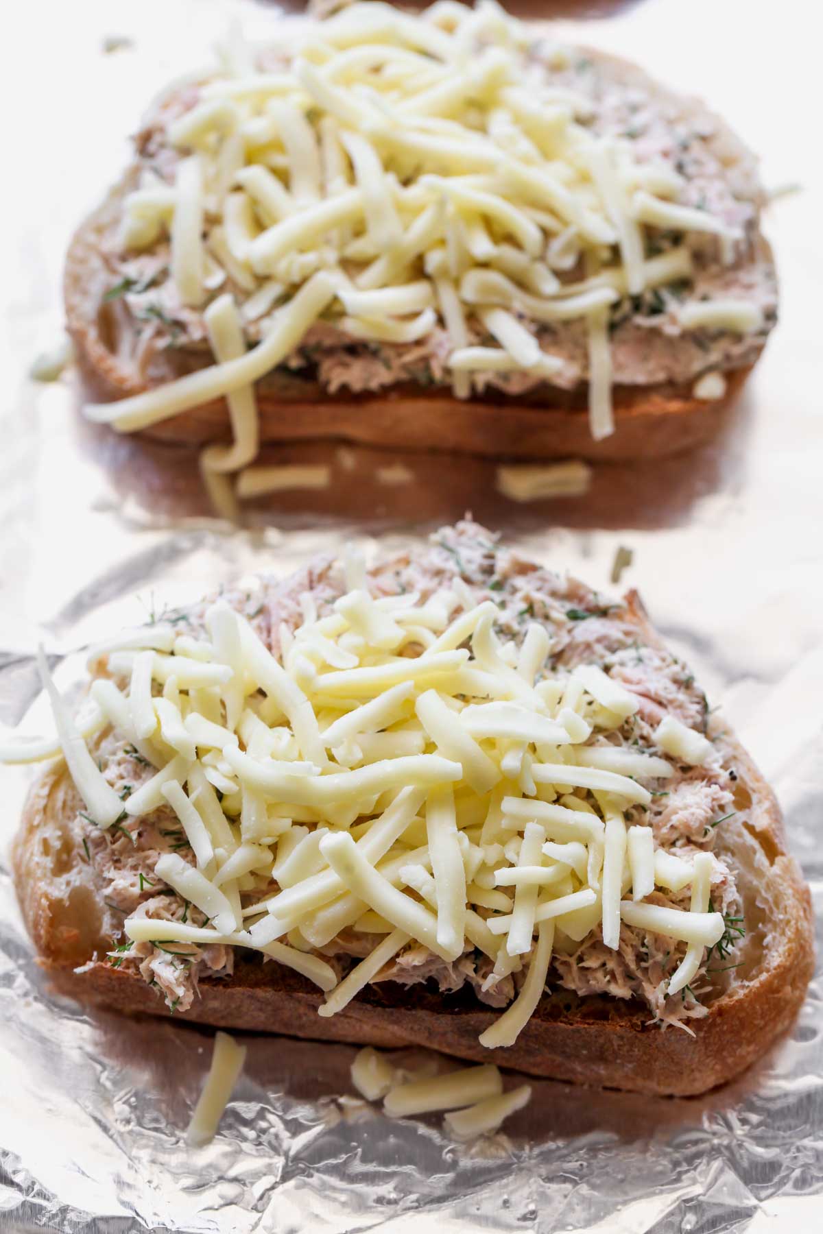 Toast topped with tuna and shredded cheese on a baking sheet