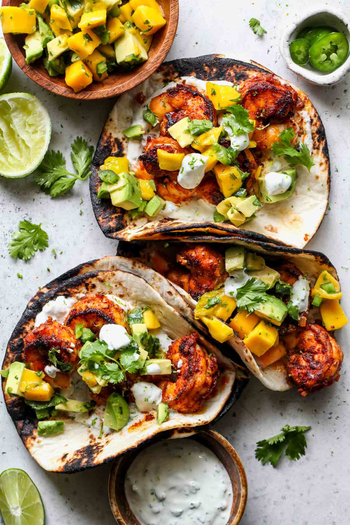 Chipotle shrimp tacos arranged on a surface with lime crema and mango salsa