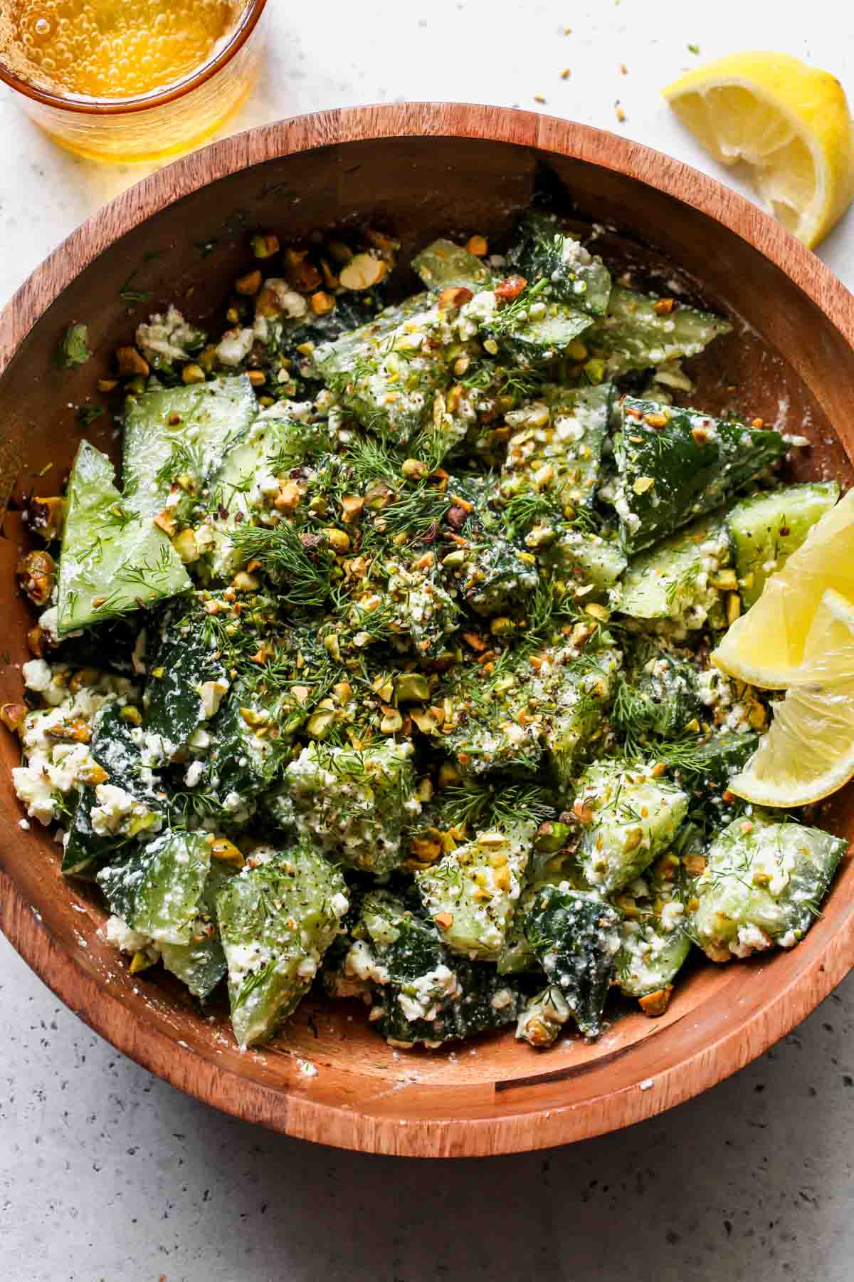 Smashed cucumber salad with feta dressing and pistachios in a wooden serving bowl.
