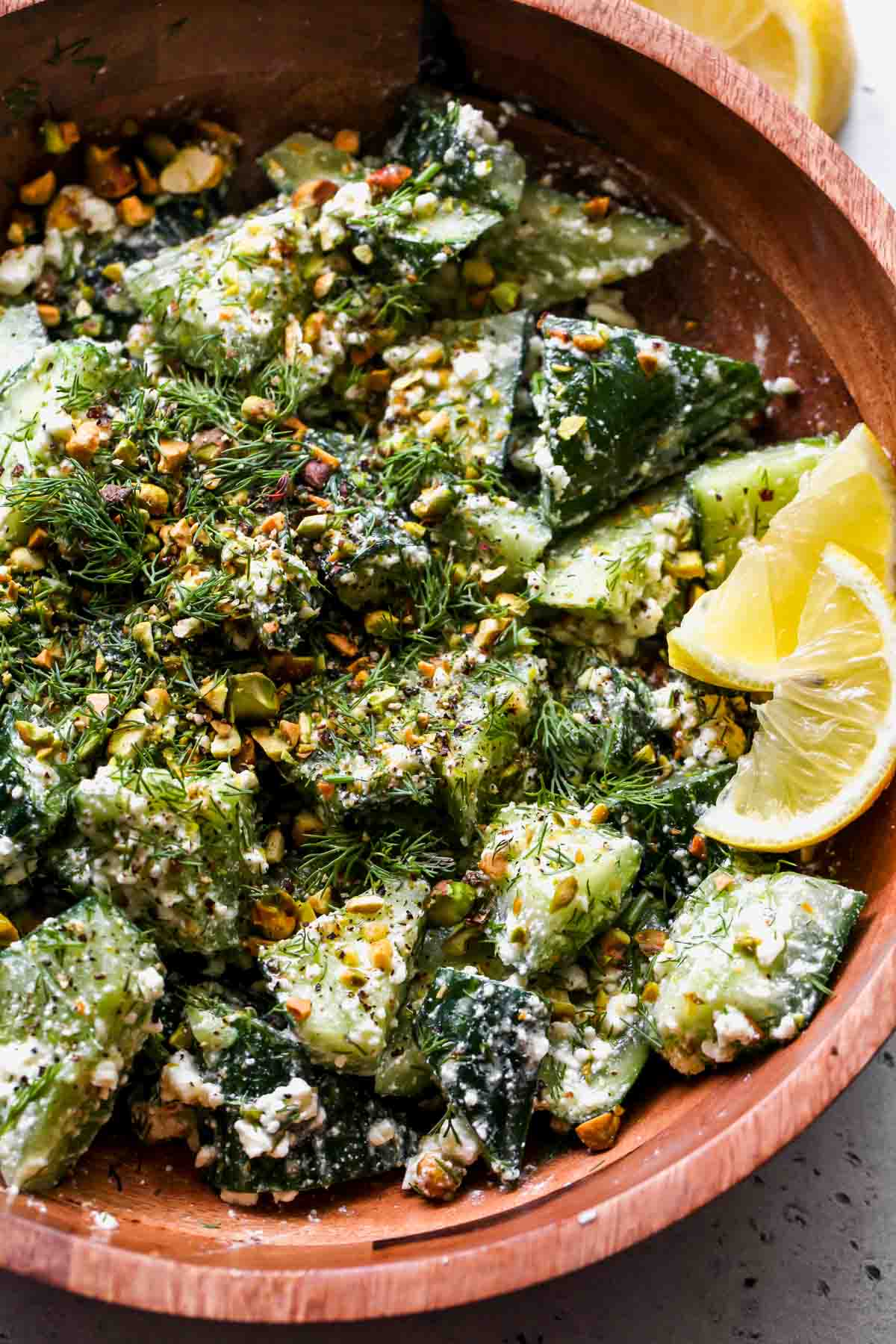 Smashed cucumbers, feta dressing, herbs, and pistachios in a wooden serving bowl.
