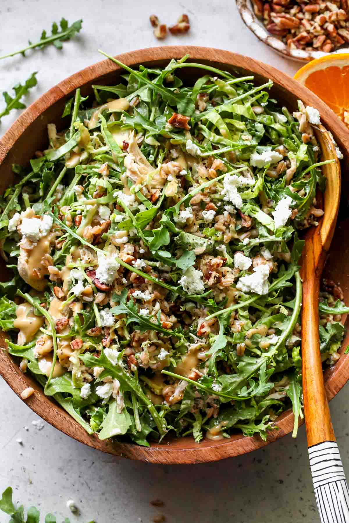 Arugula goat cheese salad tossed with honey mustard dressing in a wooden serving bowl