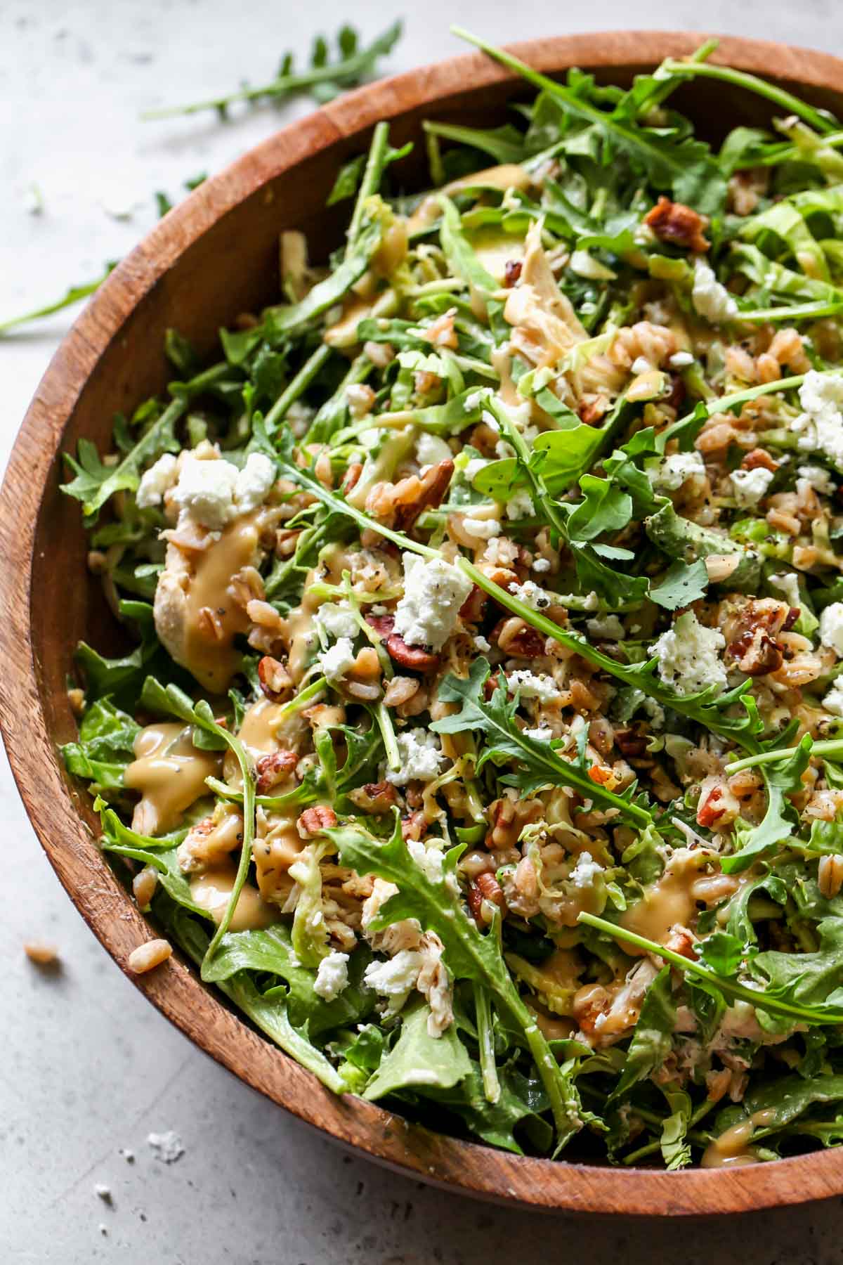 Arugula goat cheese salad tossed with farro and honey mustard dressing in a wooden bowl
