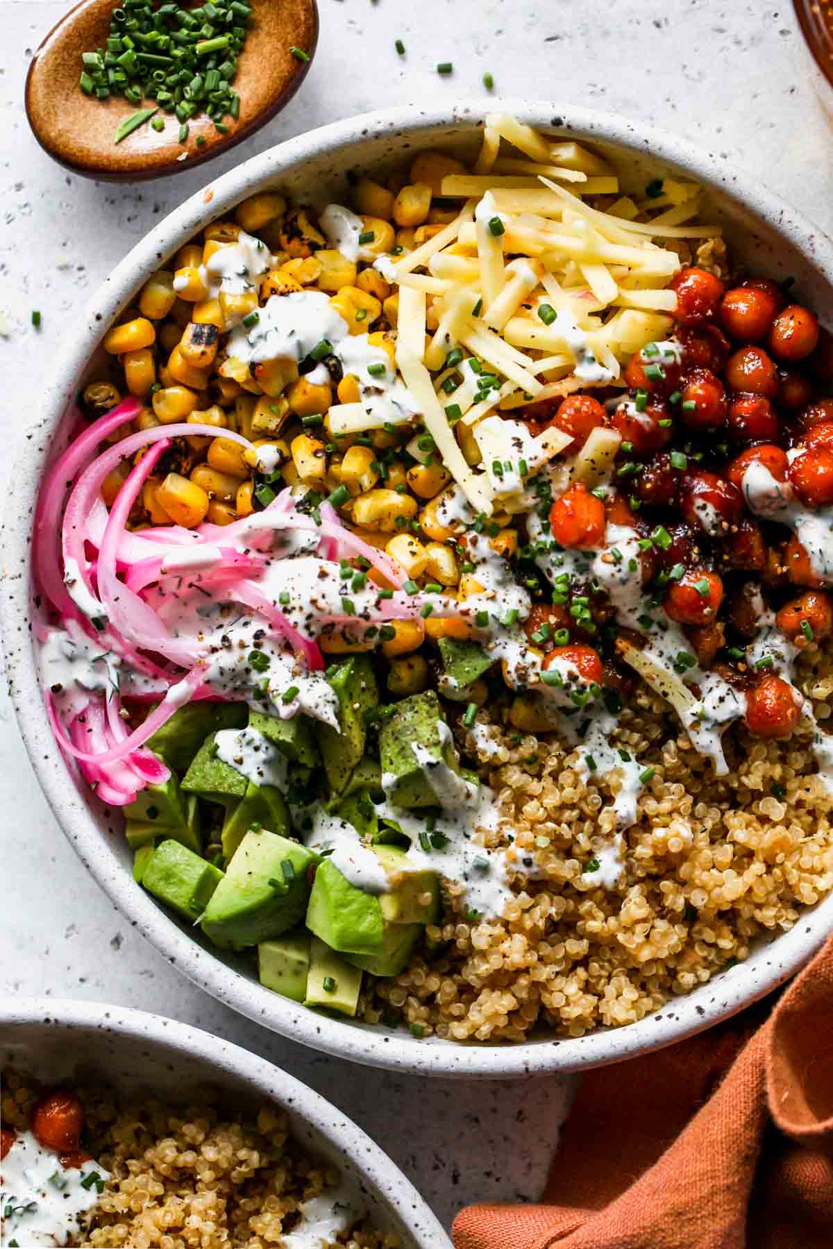 Chickpeas, quinoa, avocado, onion, and corn in a white bowl topped with yogurt ranch dressing