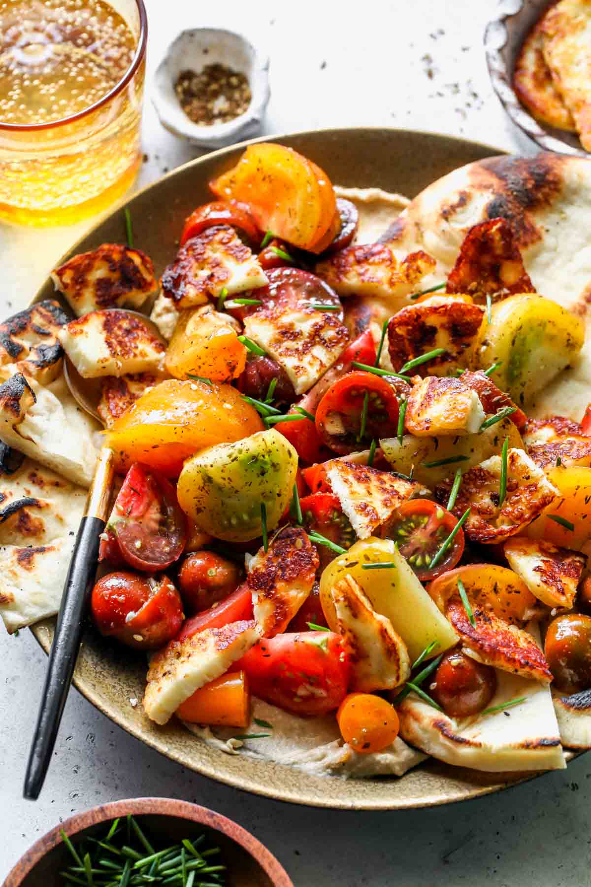 Marinated tomatoes, halloumi, hummus, and pita arranged on a gold plate