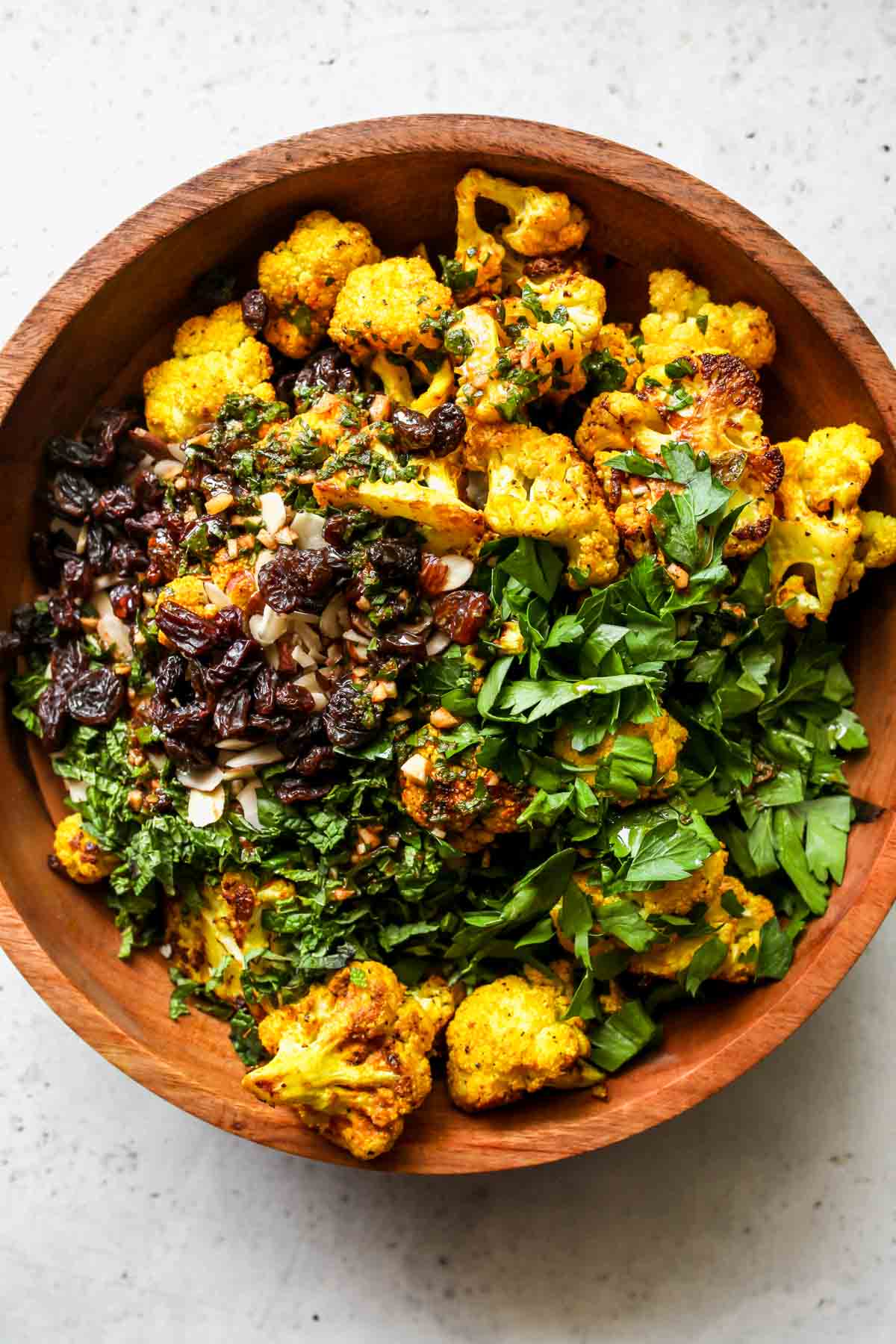 Roasted cauliflower, couscous, herbs, raisins, and almonds being mixed in a large bowl