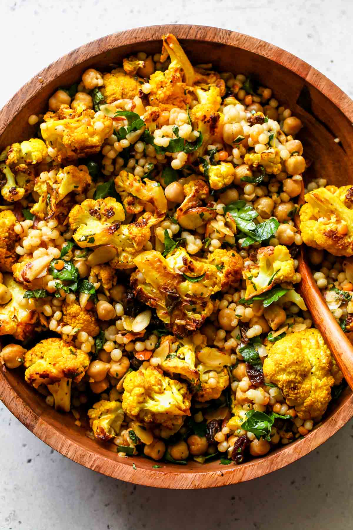 Pearl couscous salad being mixed with cauliflower and dressing in a serving bowl