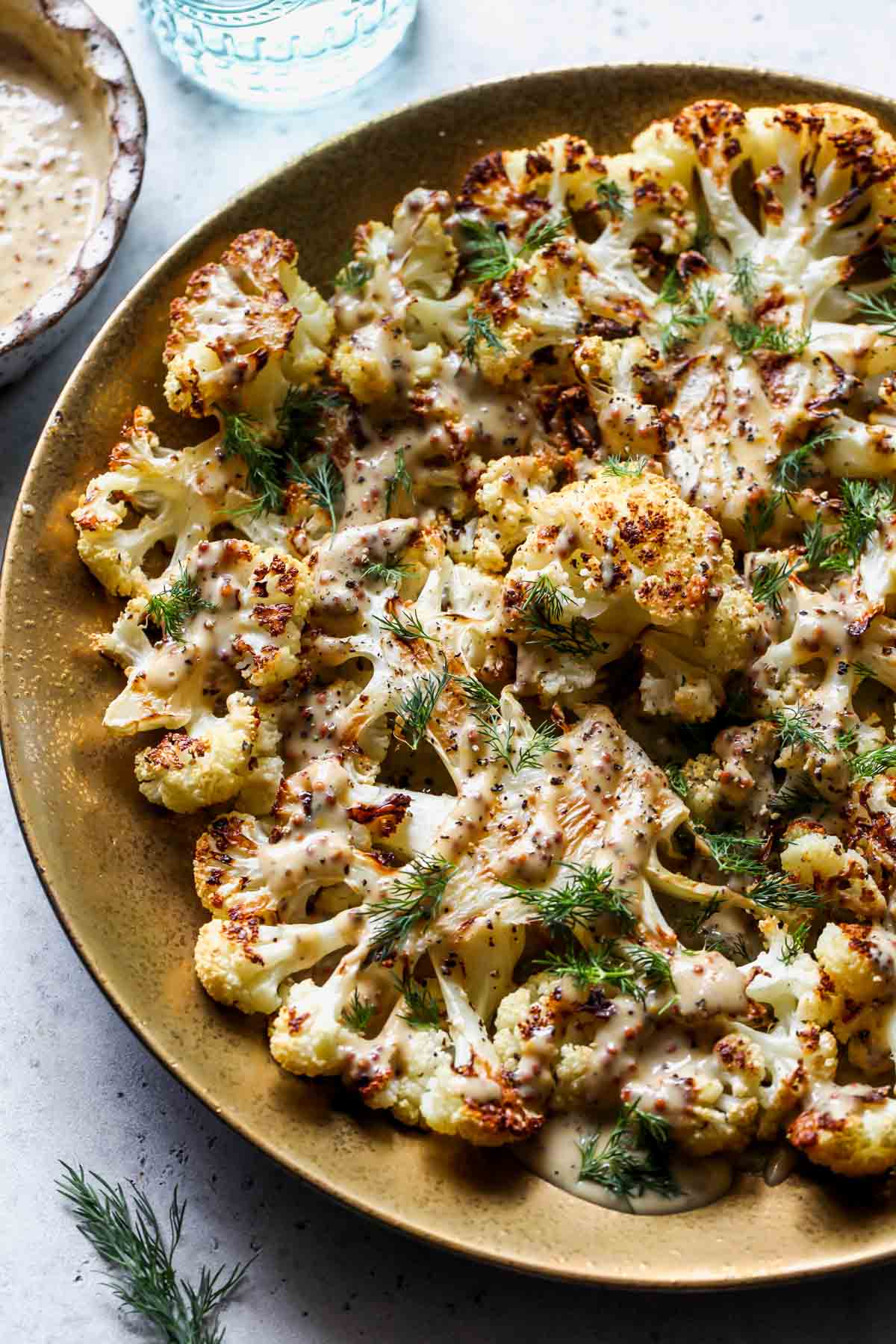 Roasted cauliflower steaks on a gold serving platter drizzled with maple-mustard sauce