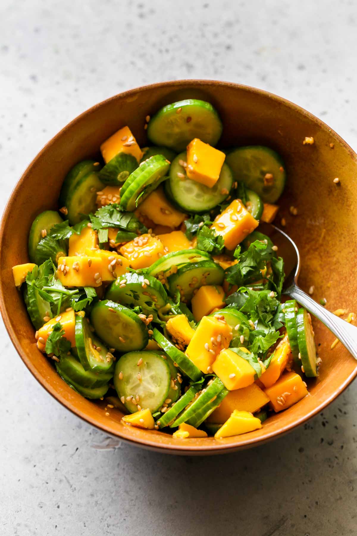 Cucumber-mango salad being mixed in a gold bowl