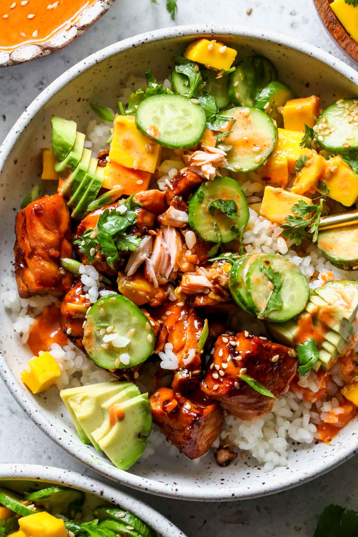 Teriyaki salmon over rice with mango salad in a white bowl