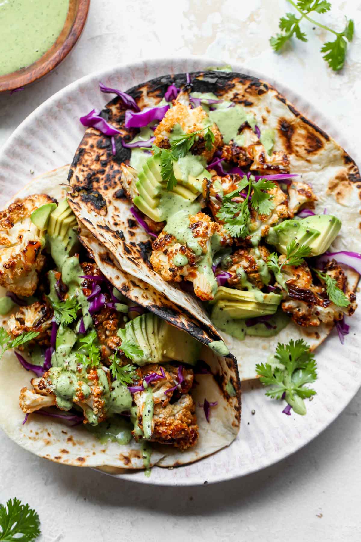 Two cauliflower tacos topped with green tahini sauce on a plate