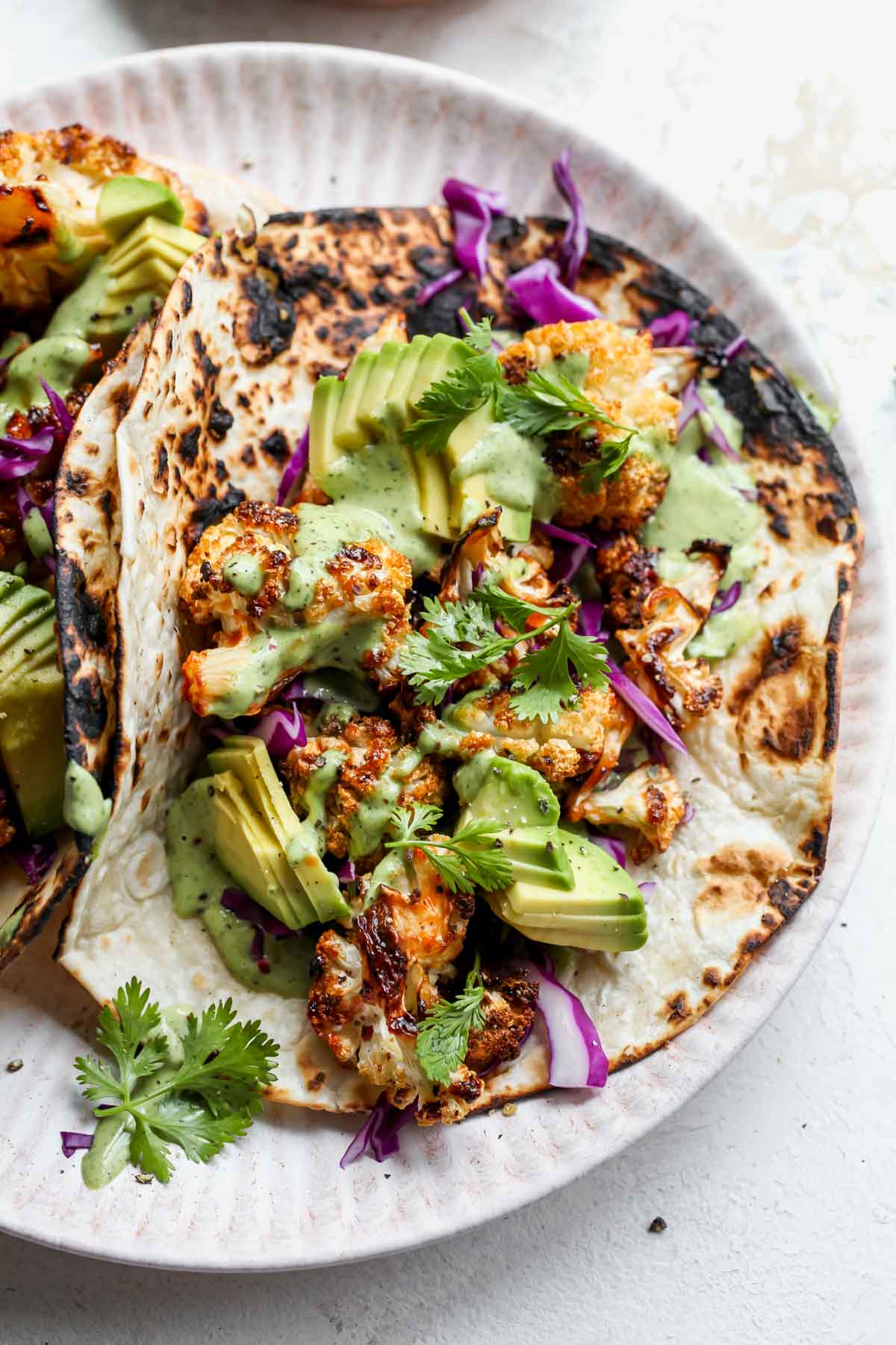 Cauliflower taco topped with green tahini sauce on a white plate