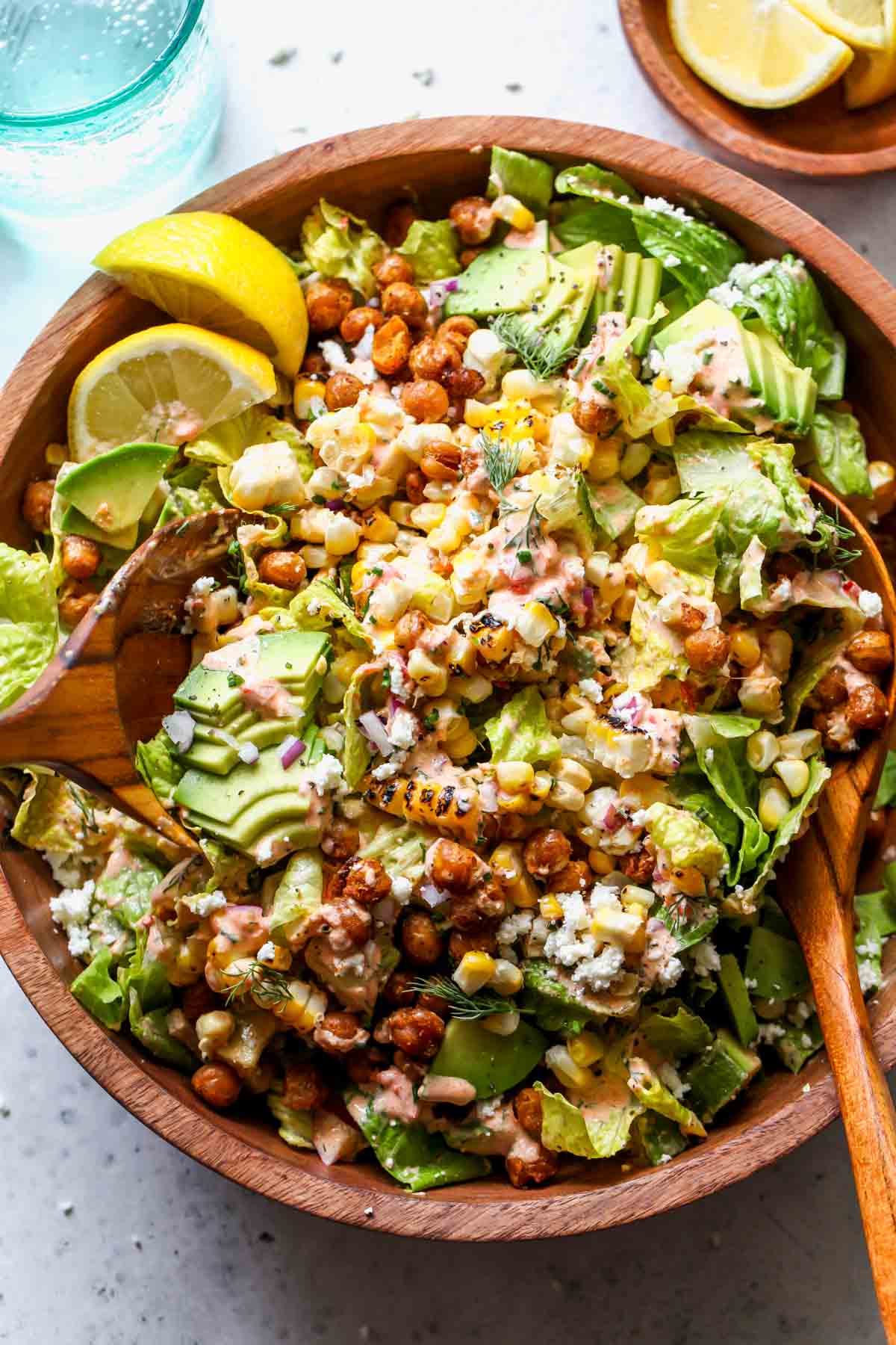 Corn and avocado salad being tossed in a wooden bowl
