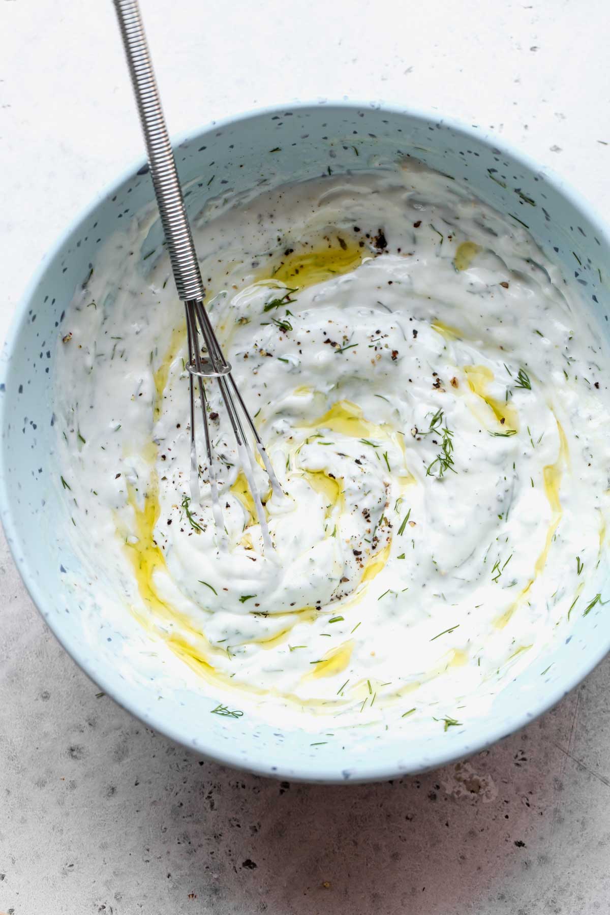 Lemon-dill yogurt sauce being whisked in a blue bowl