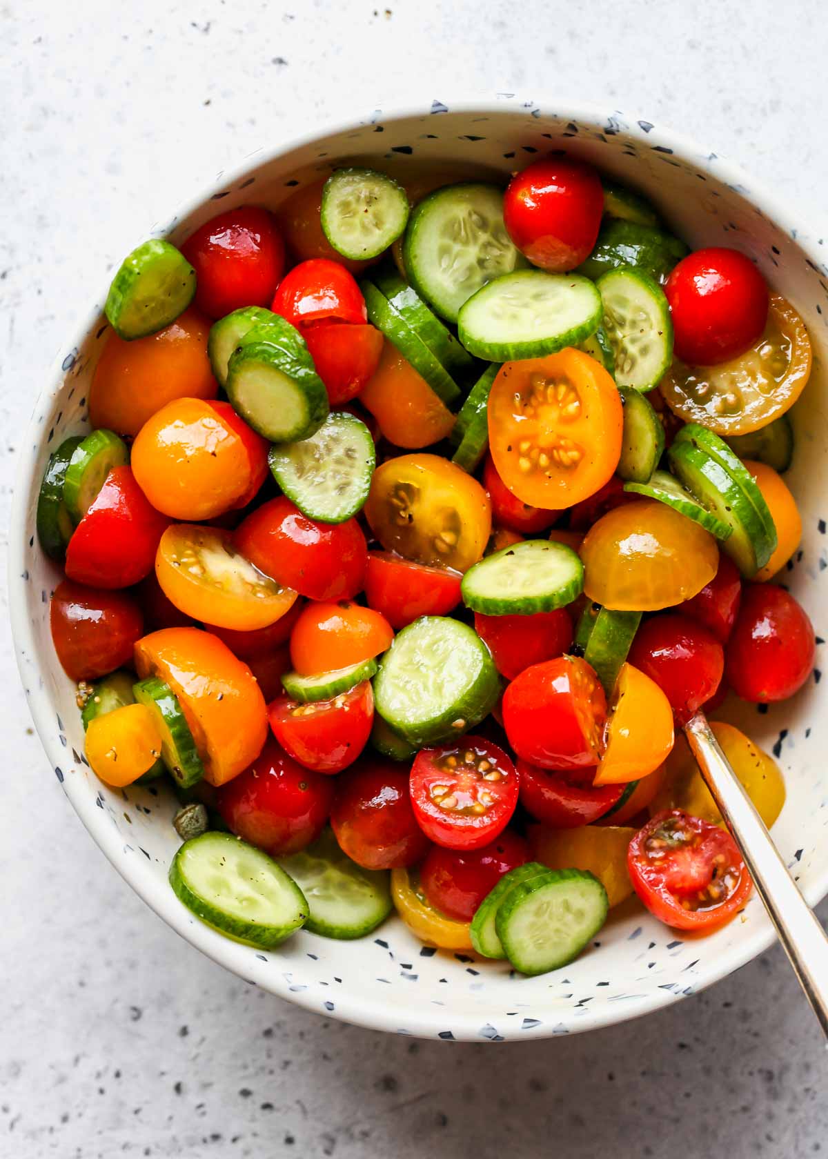 Cucumber-tomato salad being mixed in a white bowl