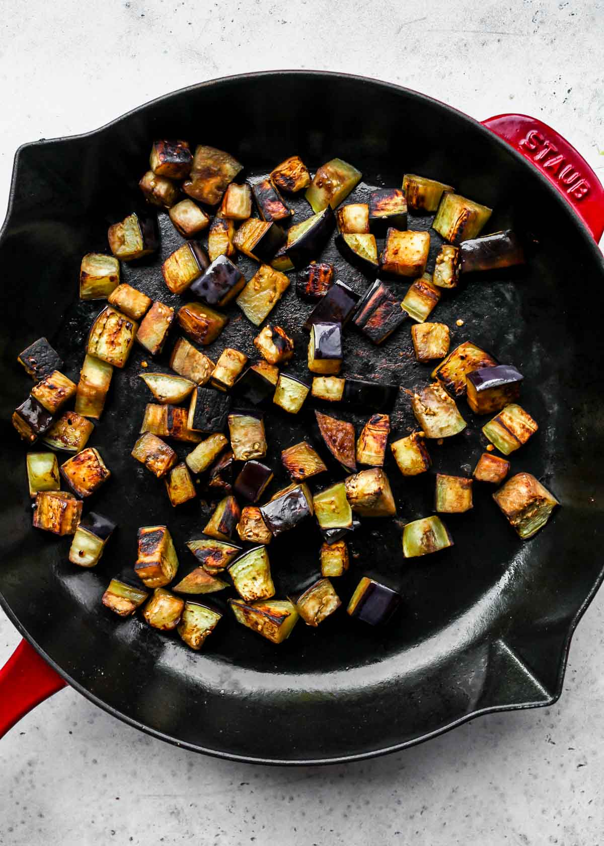 Diced eggplant being sauteed in a cast iron skillet
