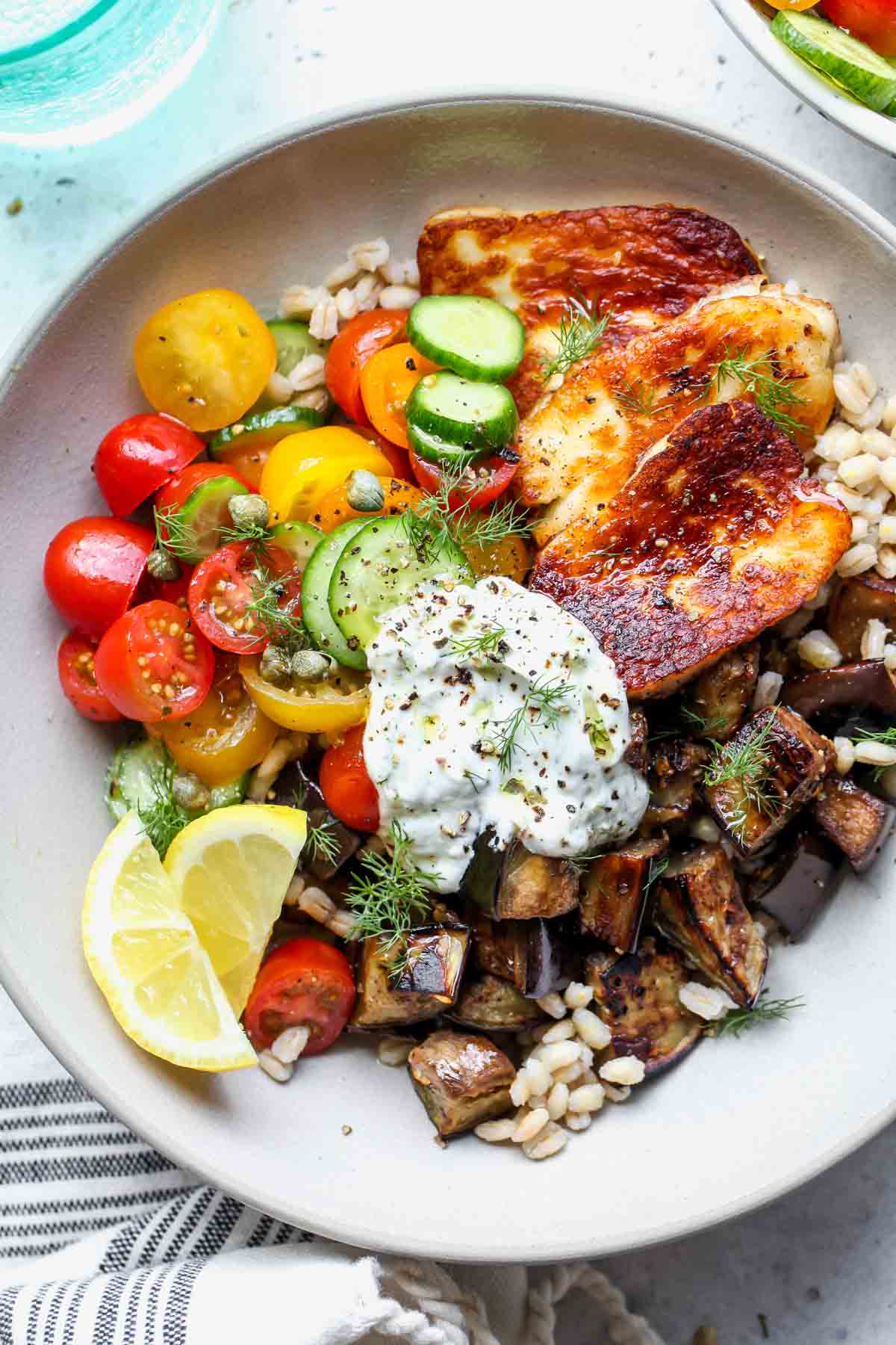 Mediterranean eggplant halloumi bowls with cucumber salad and yogurt sauce styled in a white bowl