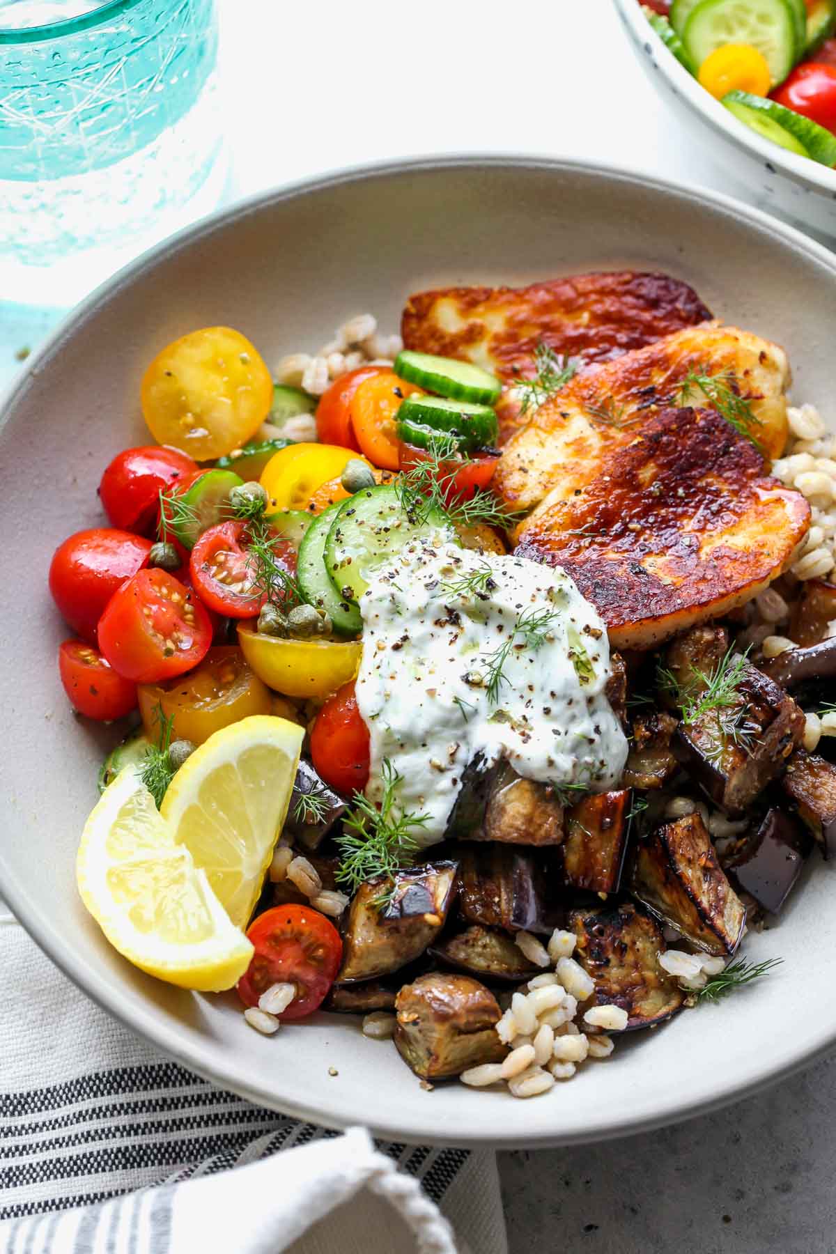 Mediterranean Eggplant and Halloumi Bowls with Lemon-Dill Sauce topped with fresh herbs in a serving bowl