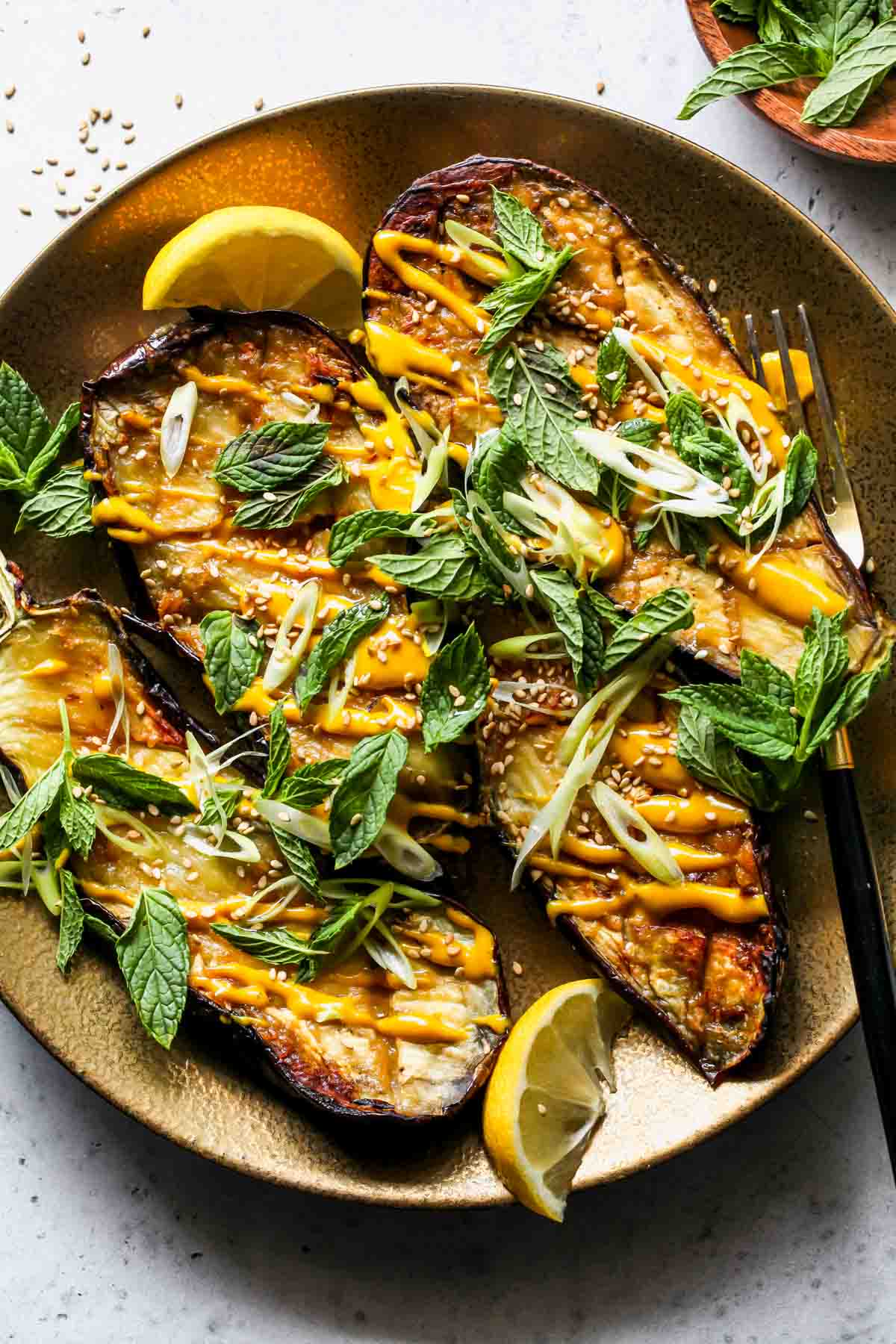 Miso roasted eggplant on a platter drizzled with tahini sauce and fresh herbs