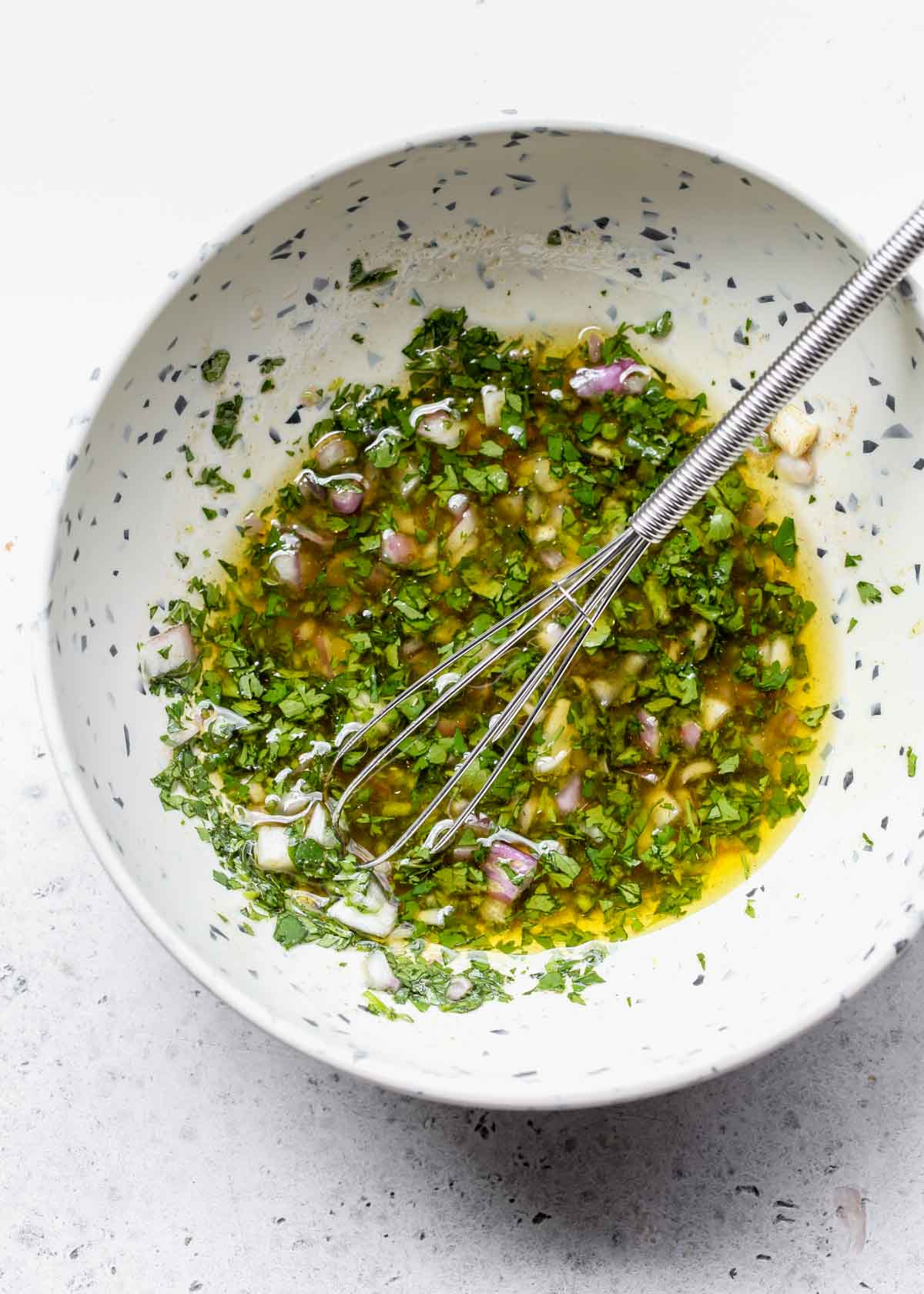 Cumin, cilantro, olive oil, shallots, and vinegar being whisked in a bowl