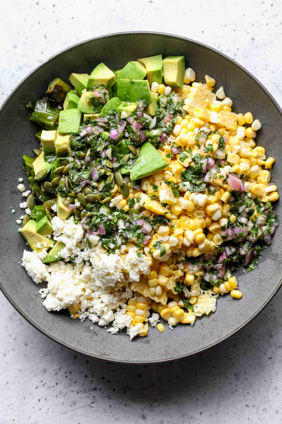 Shishito peppers, corn, avocado, cheese, and pumpkin seeds in a large bowl