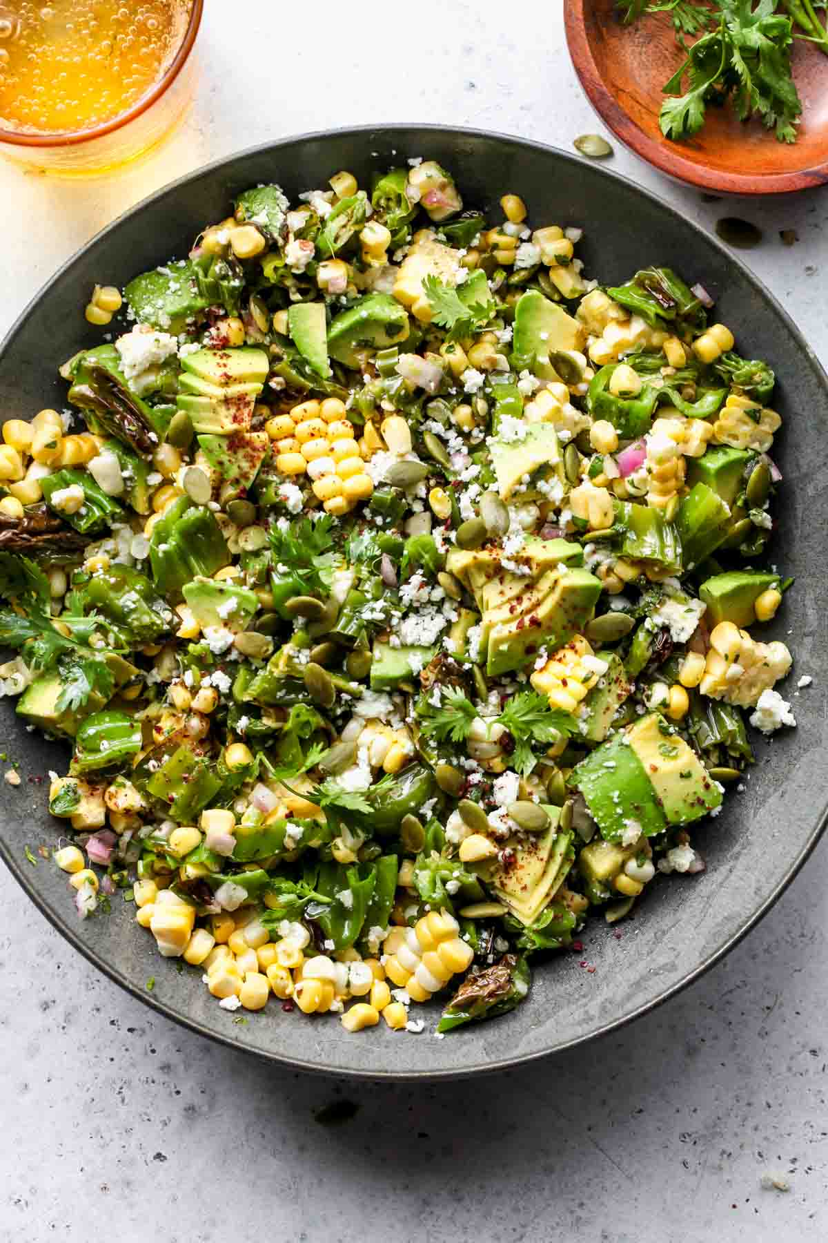 Shishito and corn salad topped with avocado and cheese in a grey serving bowl