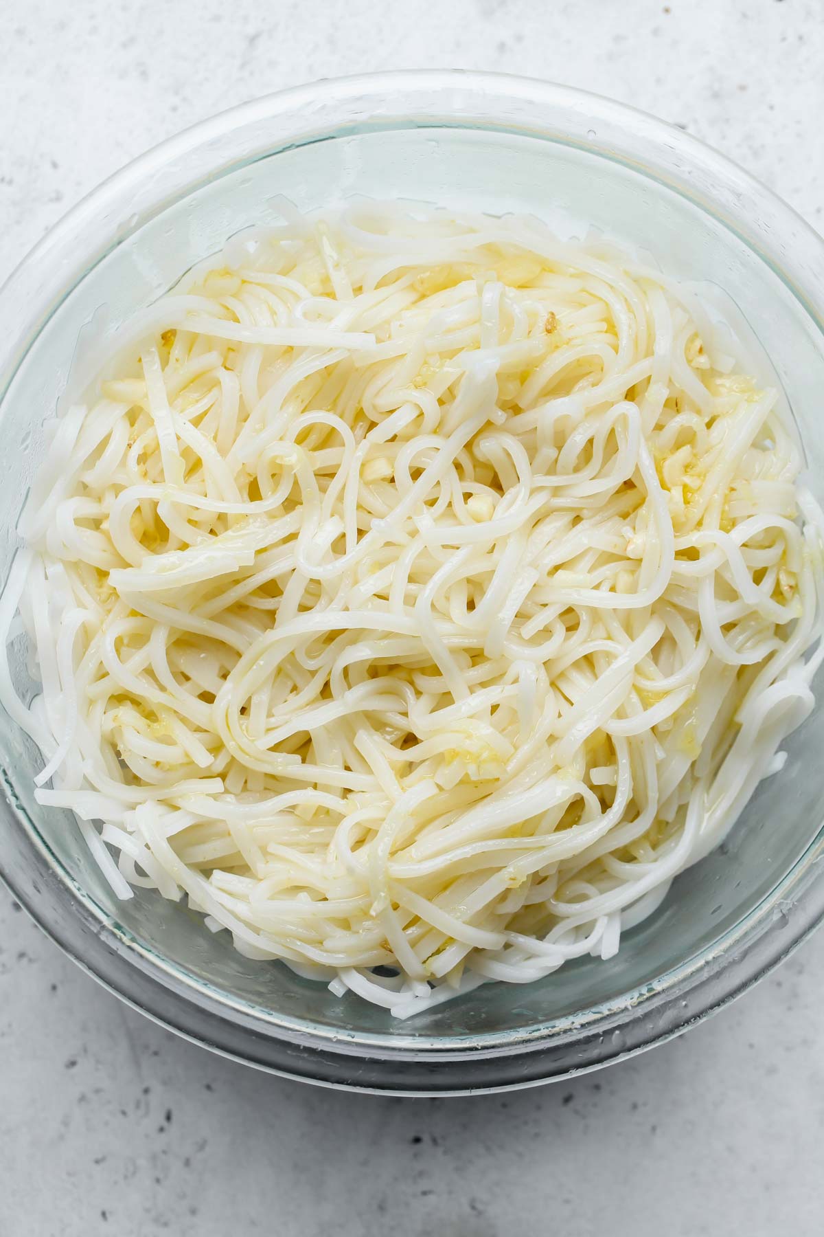 Cooked noodles being tossed in dressing in a mixing bowl