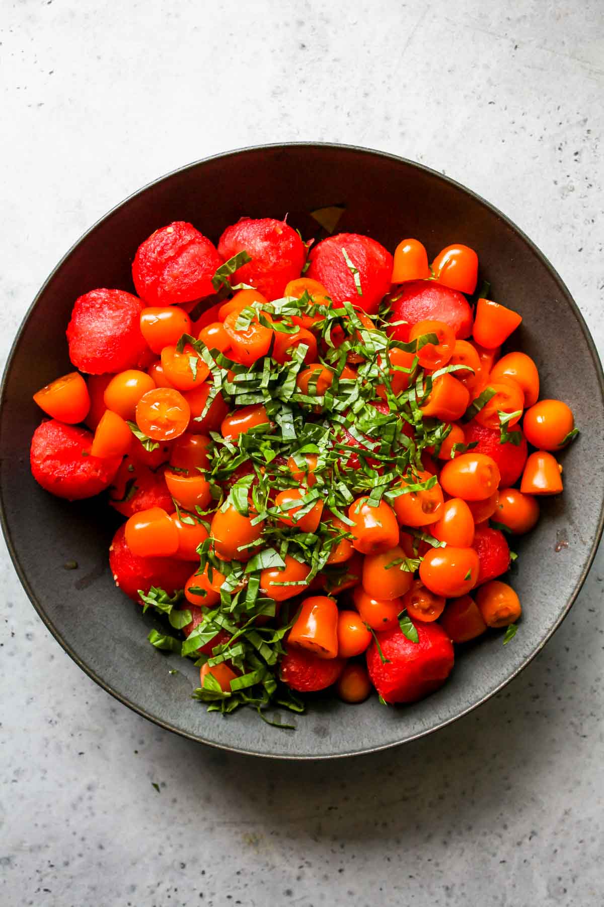 Watermelon balls, tomatoes, and basil in a mixing bowl