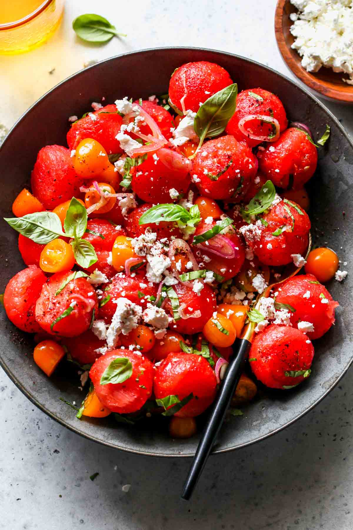 Watermelon tomato salad being tossed with dressing in a dark bowl