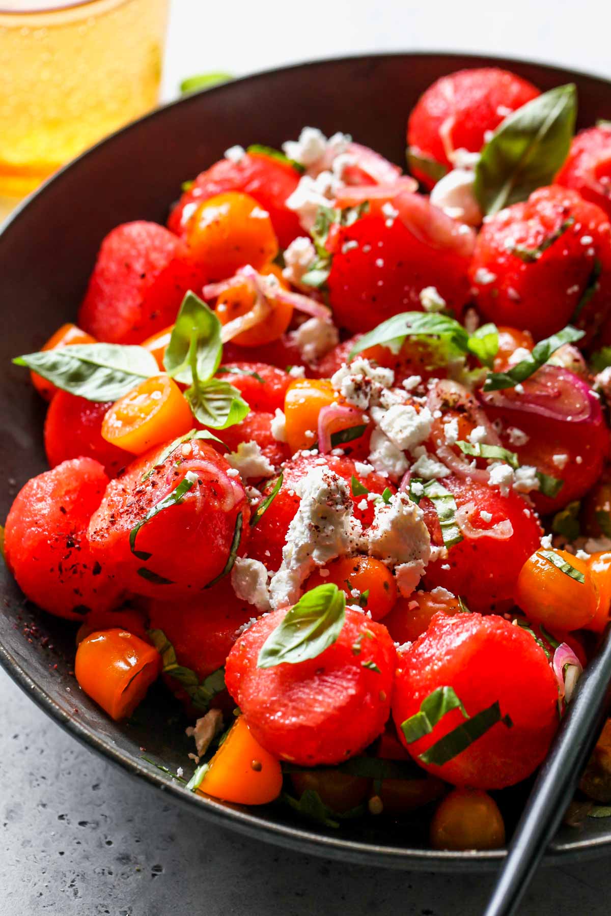 Watermelon basil salad tossed with champagne dressing being served in a bowl with a slotted spoon