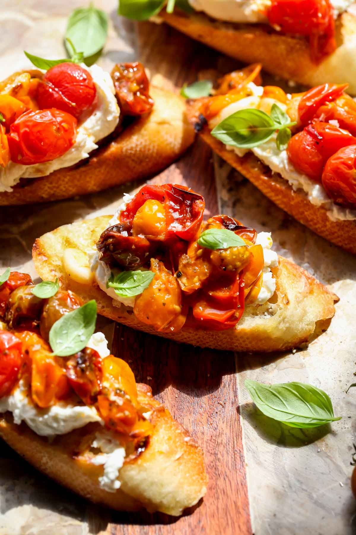 Roasted cherry tomato bruschetta topped with fresh basil arranged on a serving board