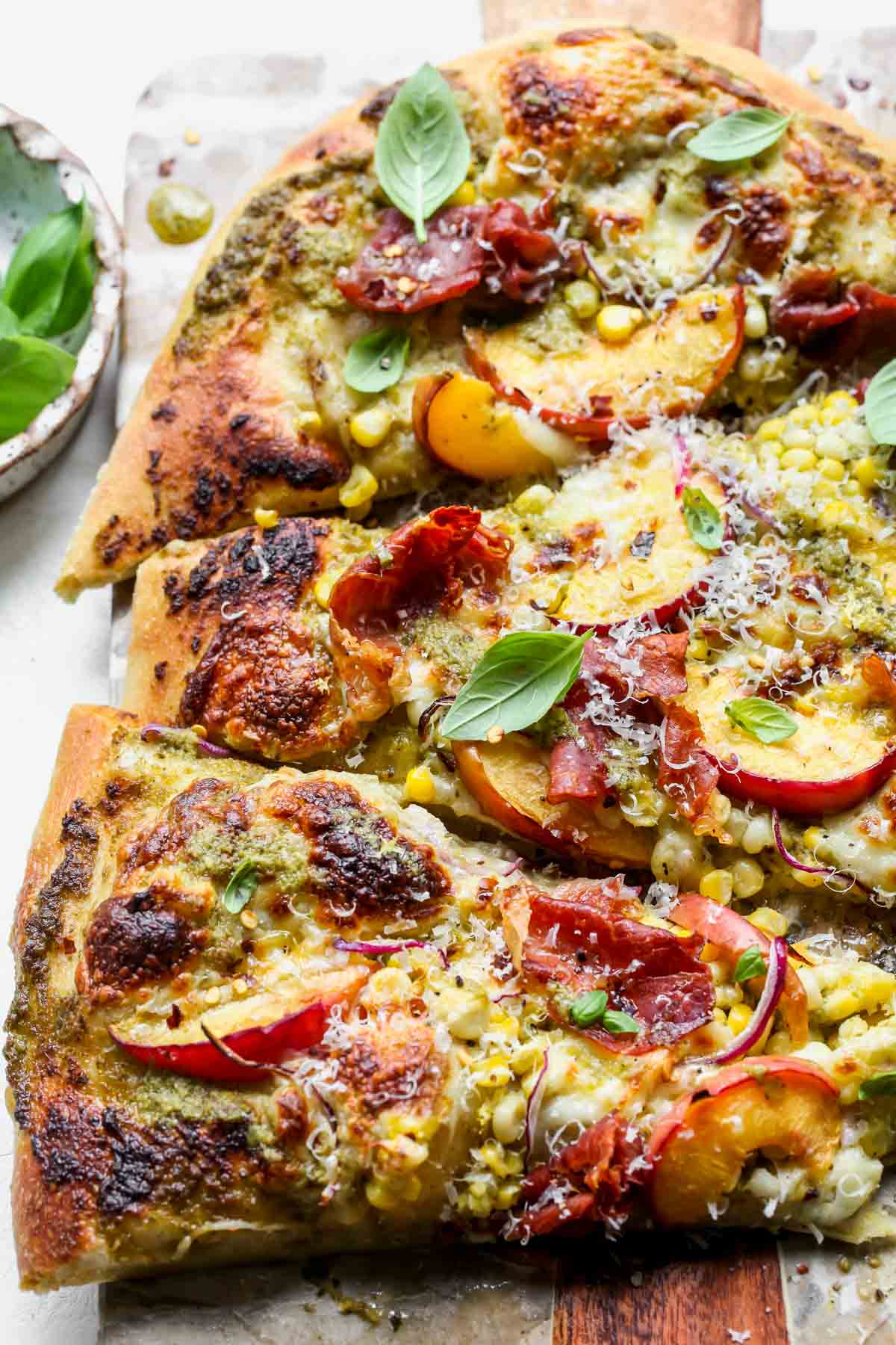 Summer pizza topped with corn, peaches, prosciutto, and fresh basil