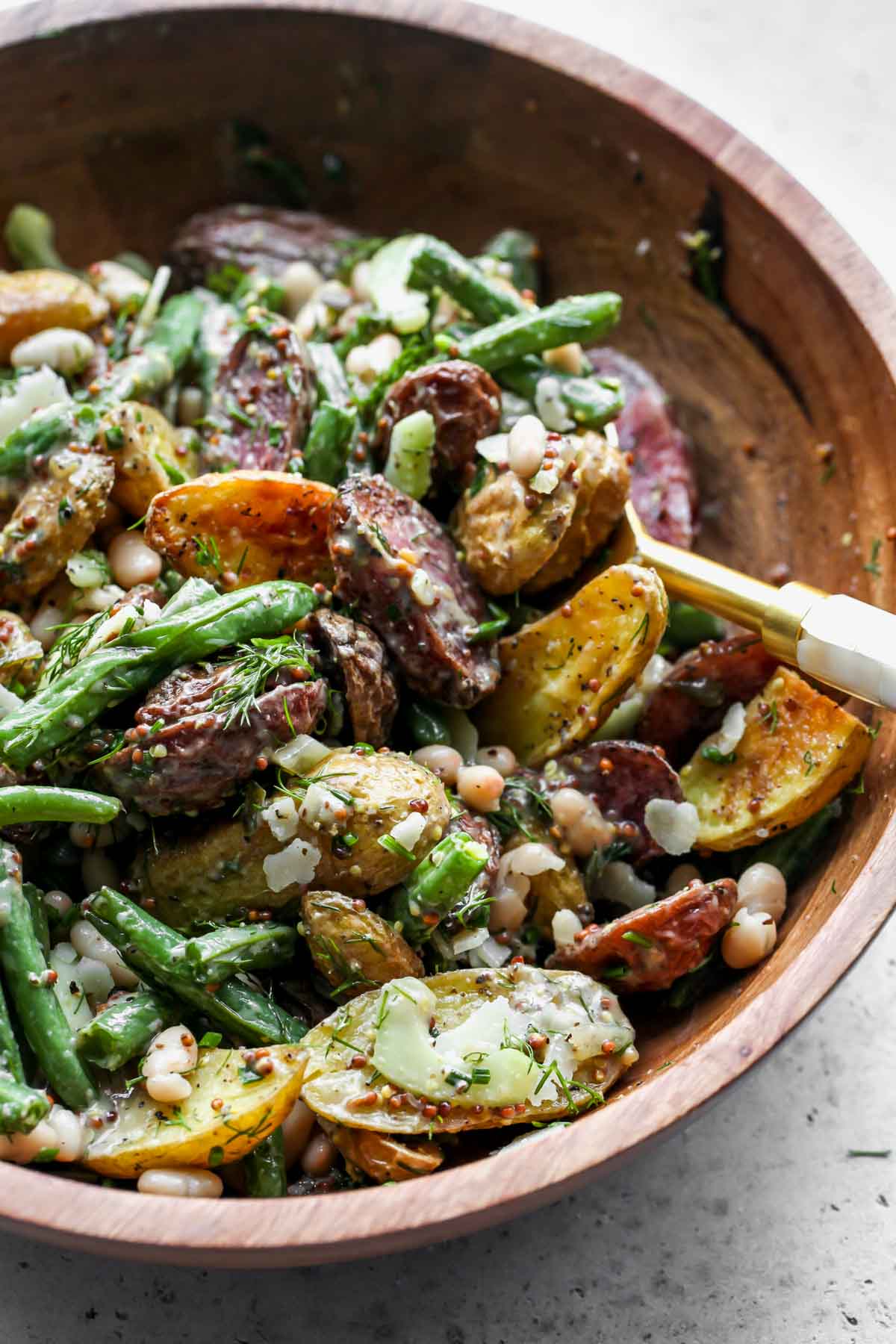 Potatoes, green beans, white beans, and mustard dressing being tossed in a bowl