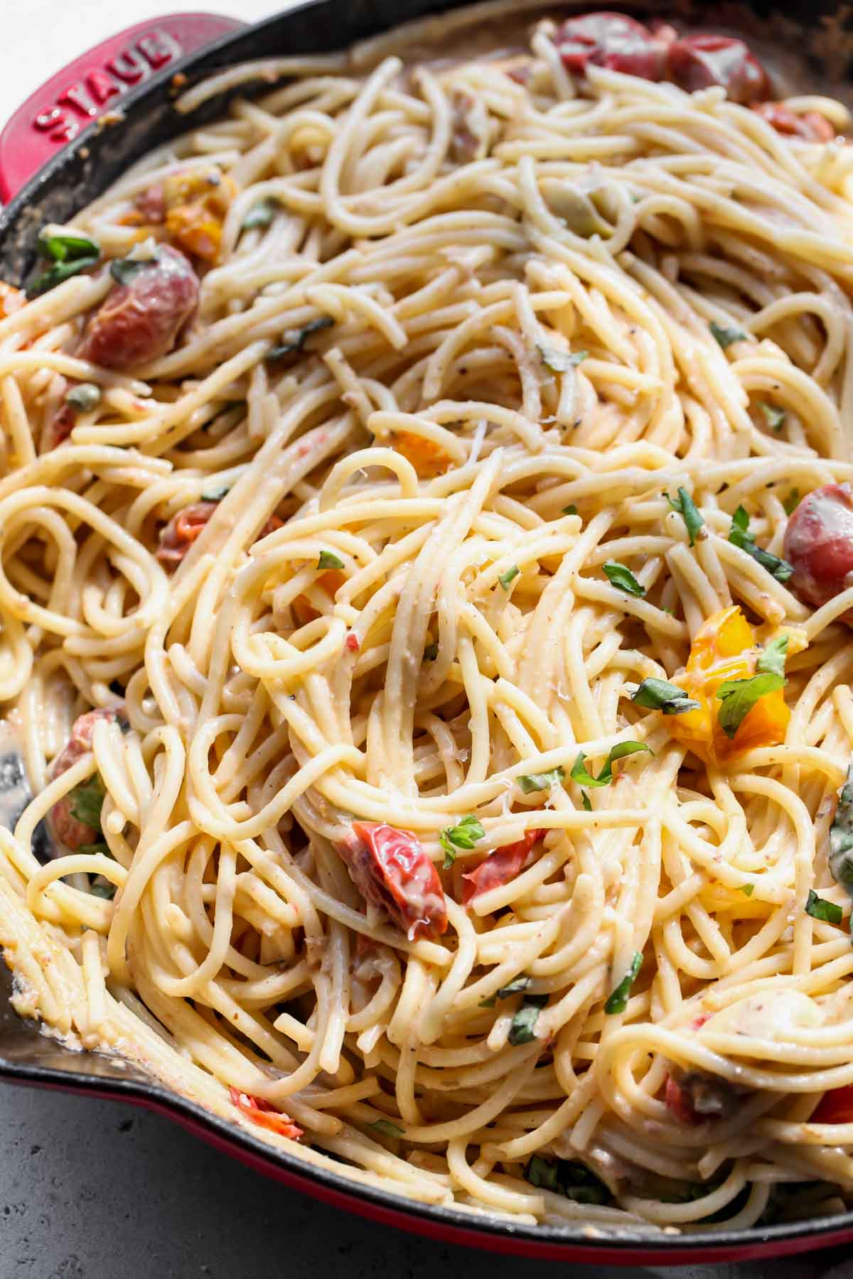 Spaghetti being tossed in tahini pasta sauce in a skillet.