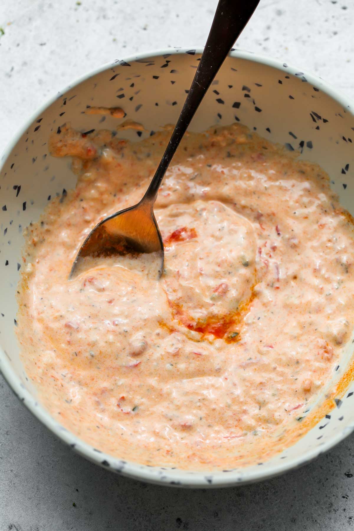 Tzatziki and harissa being mixed in a white bowl