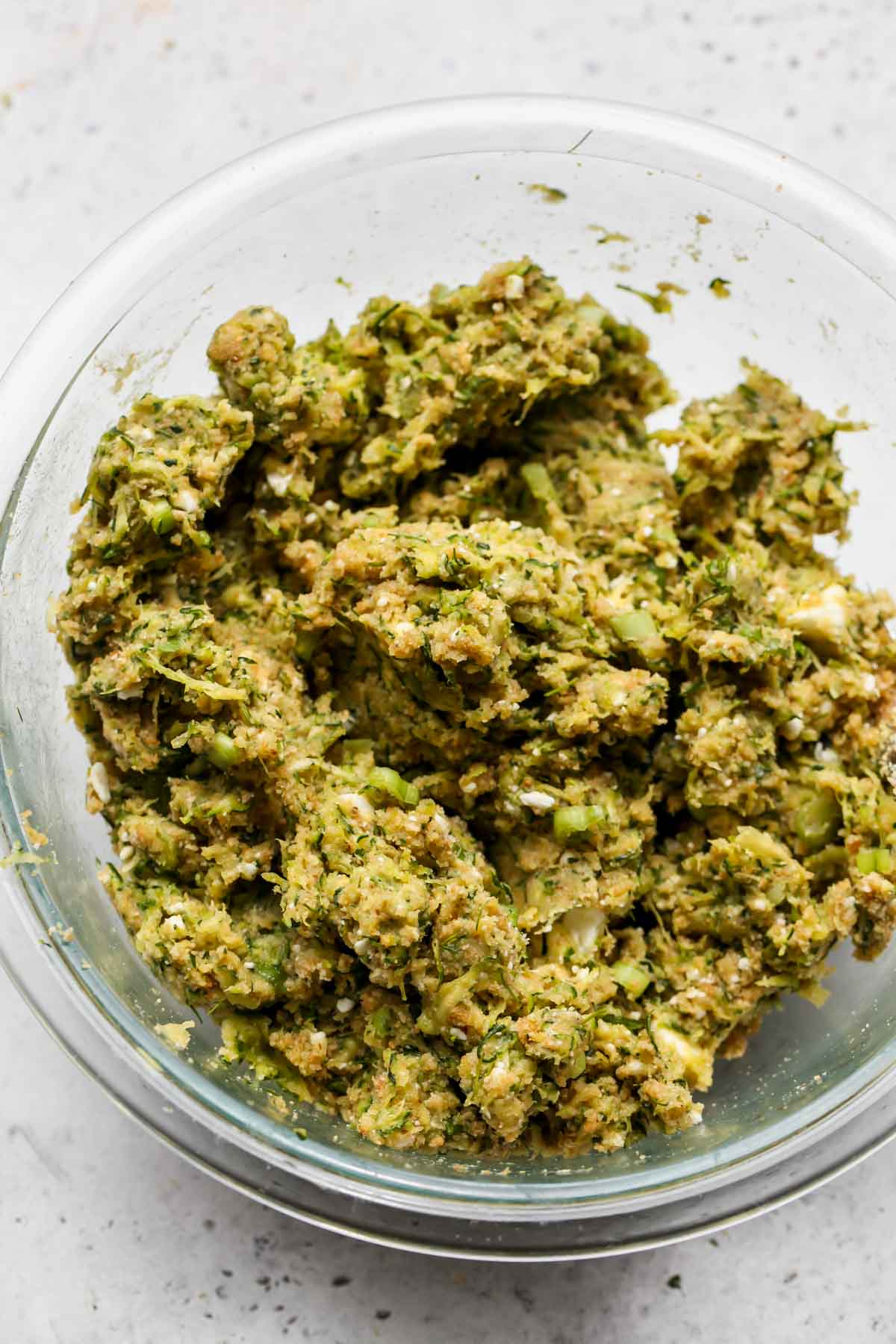 Zucchini shreds being mixed with breadcrumbs, eggs, and spices