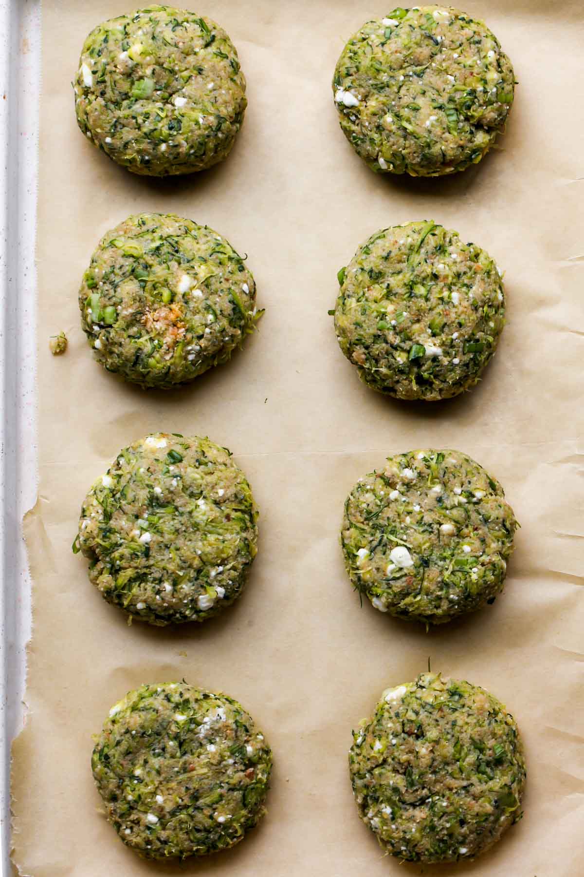 Zucchini mixture being formed into cakes and arranged on a parchment-lined baking sheet
