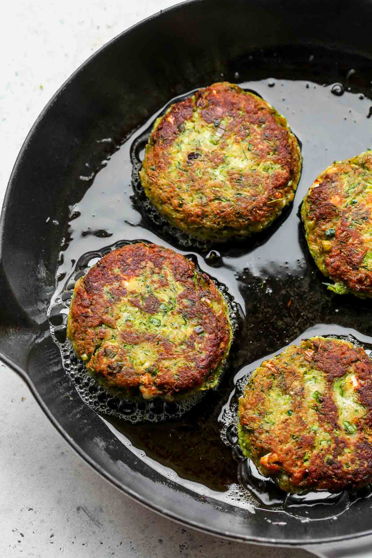 Zucchini cakes being fried in a cast iron skillet