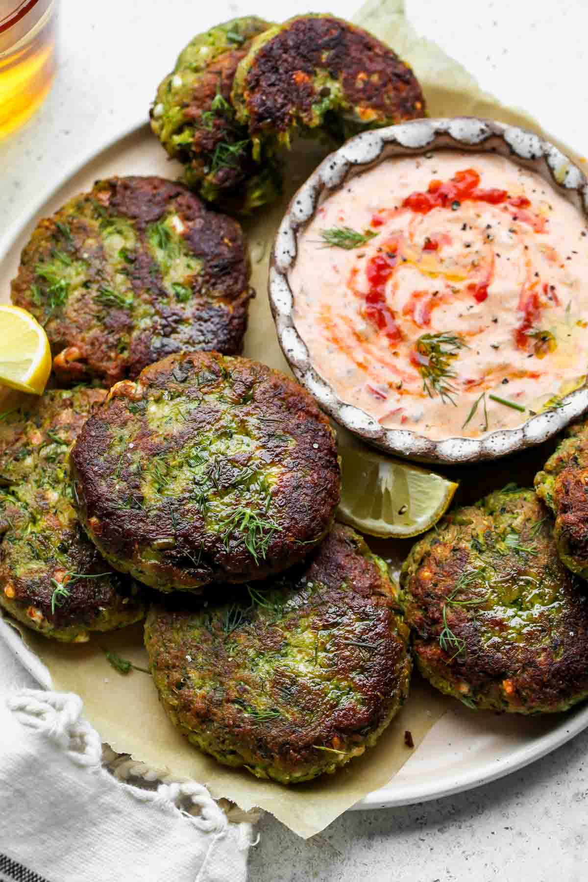 Zucchini cakes arranged on a platter with a bowl of harissa tzatziki