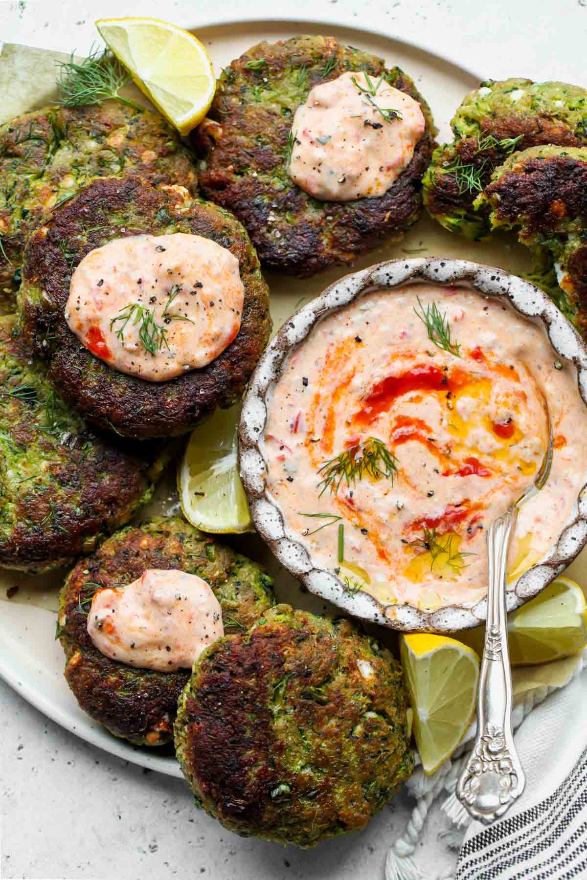 Zucchini feta cakes topped with harissa tzatziki arranged on a serving platter
