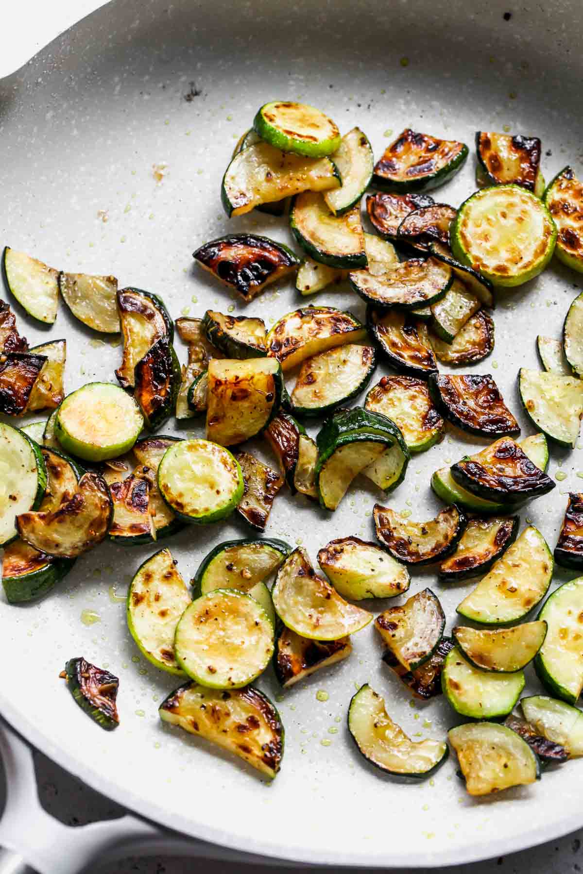 Sliced zucchini being sauteed in a white skillet