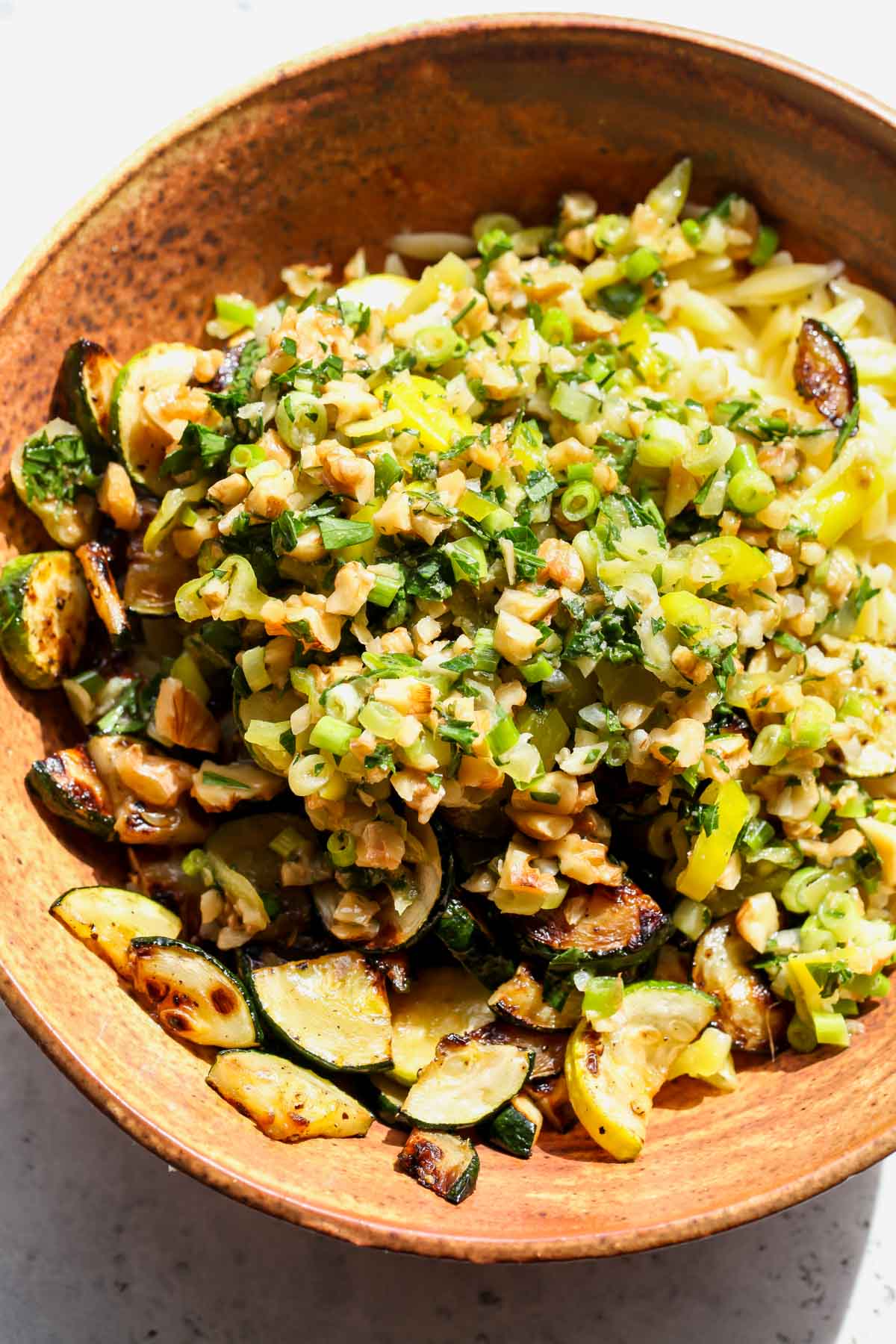 Orzo, zucchini, and Pepperoncini Dressing being combined in a brown mixing bowl